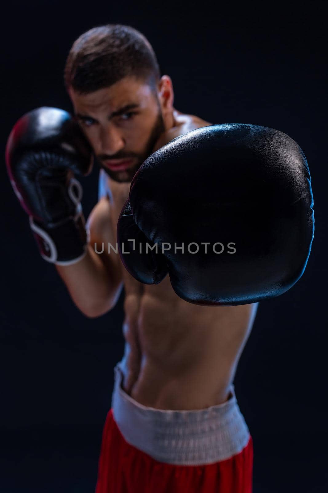 Portrait of tough male boxer posing in boxing stance against black background. Professional fighter ready for boxing match.