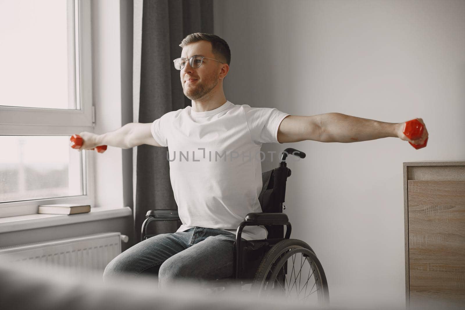 Young man in wheel-chair doing exercises indoors by prostooleh