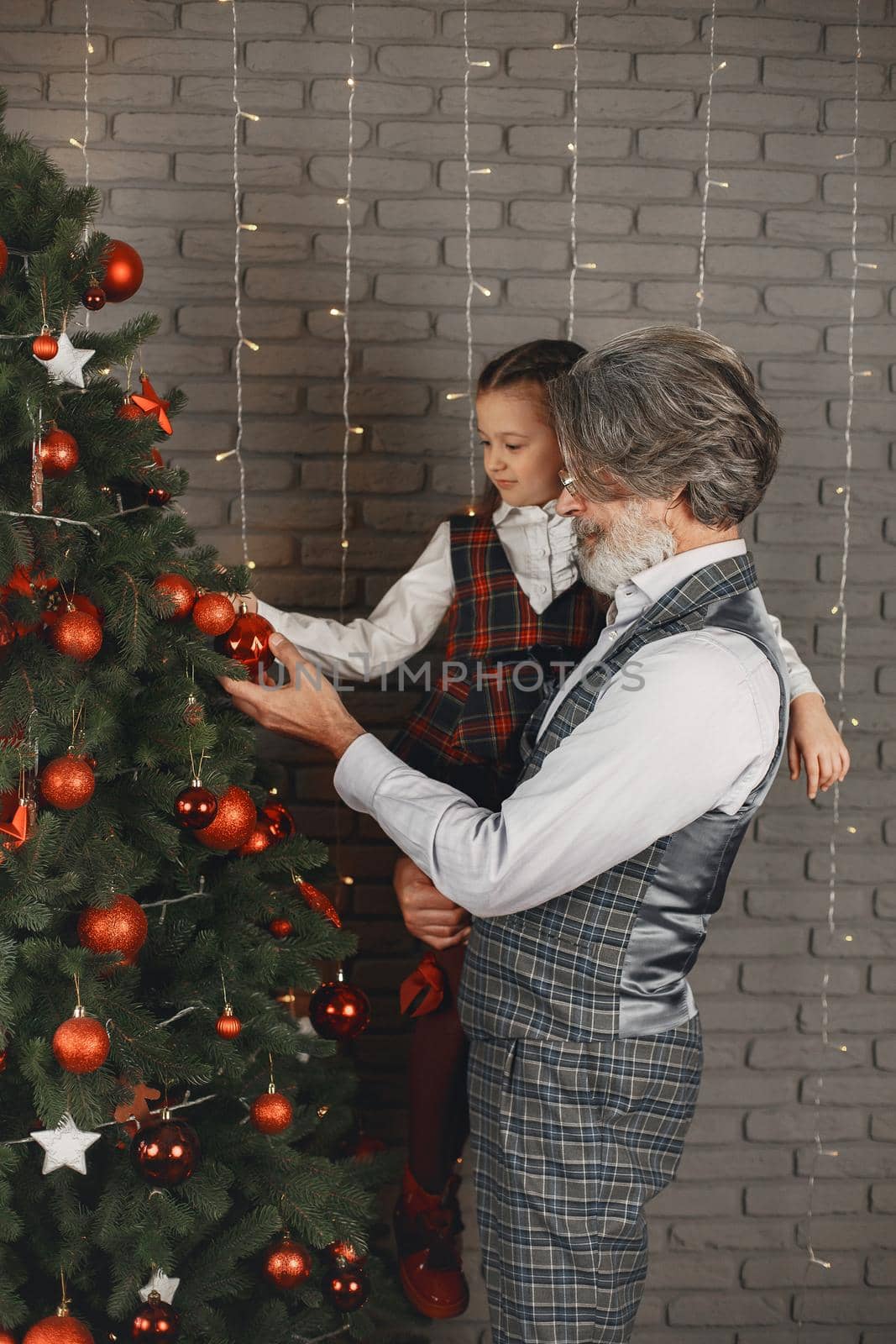 Smiling grandfather and granddaughter decorate the Christmass rtee by prostooleh