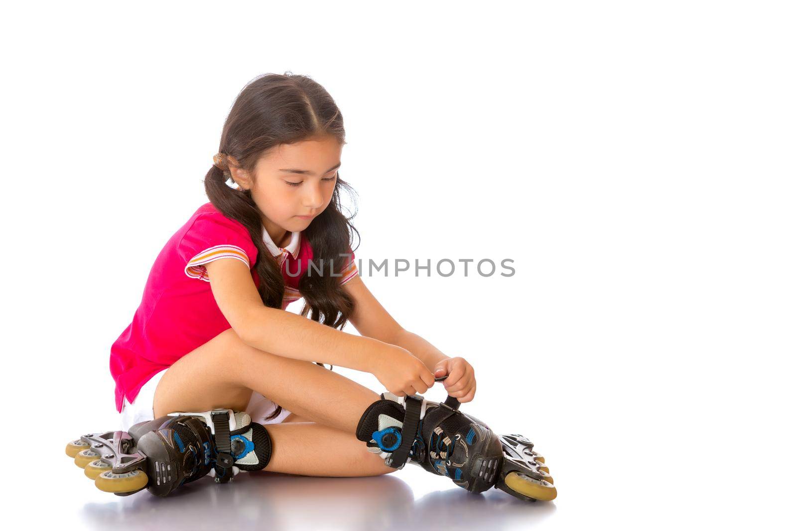 Beautiful little Asian girl puts on roller skates. The concept of advertising sports goods, a healthy lifestyle. Isolated on white background.