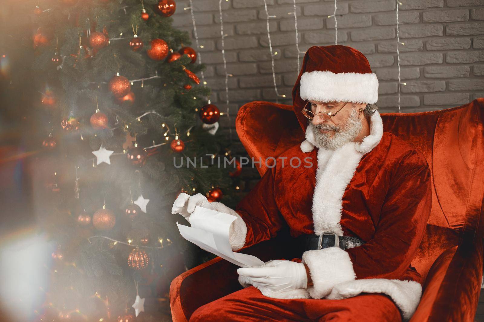 Santa Claus having a rest by the Christmass tree. Home decoration. Santa with letter from children.