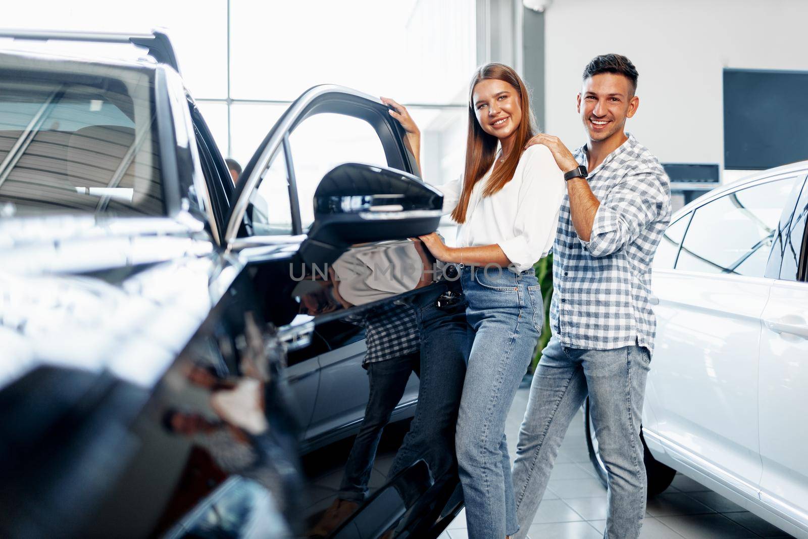 Young happy couple just bought a new car in a dealership showroom