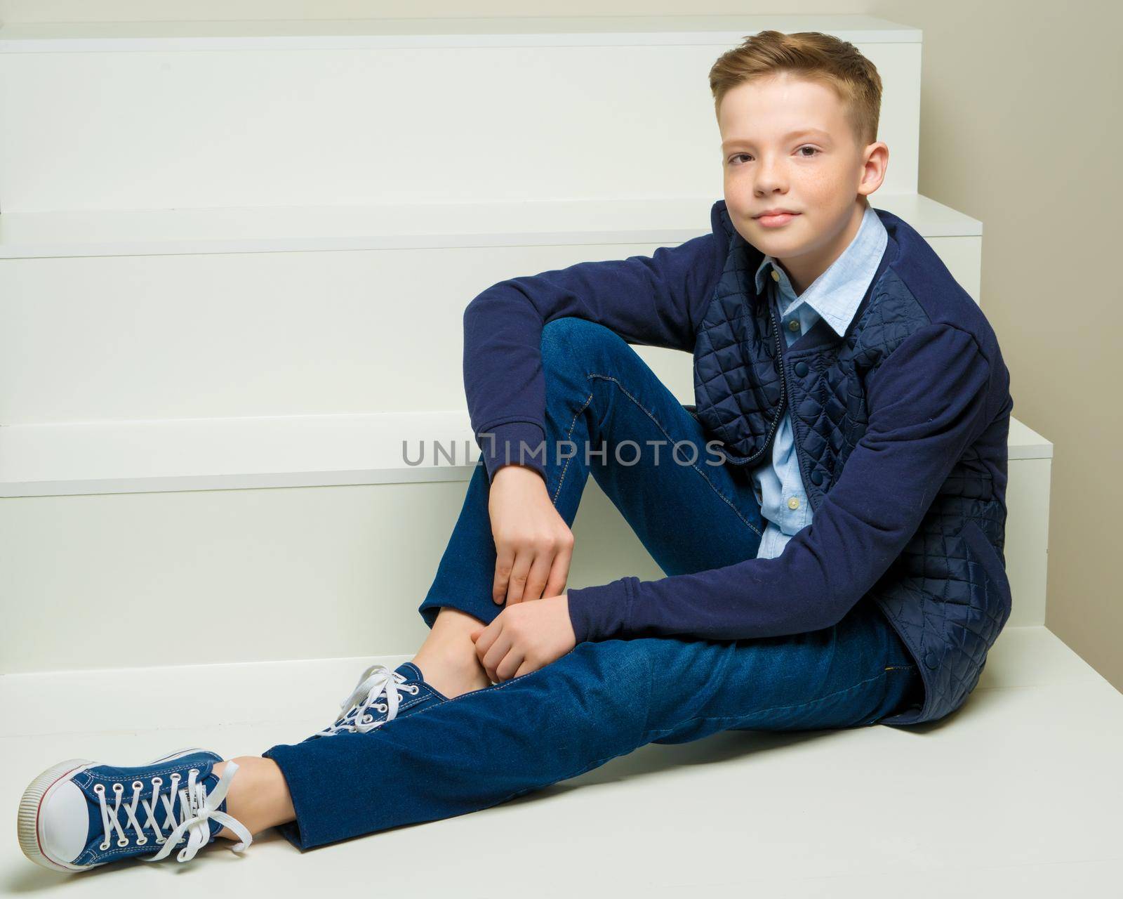 A handsome school-age boy sits on a white staircase. The concept of youth culture.