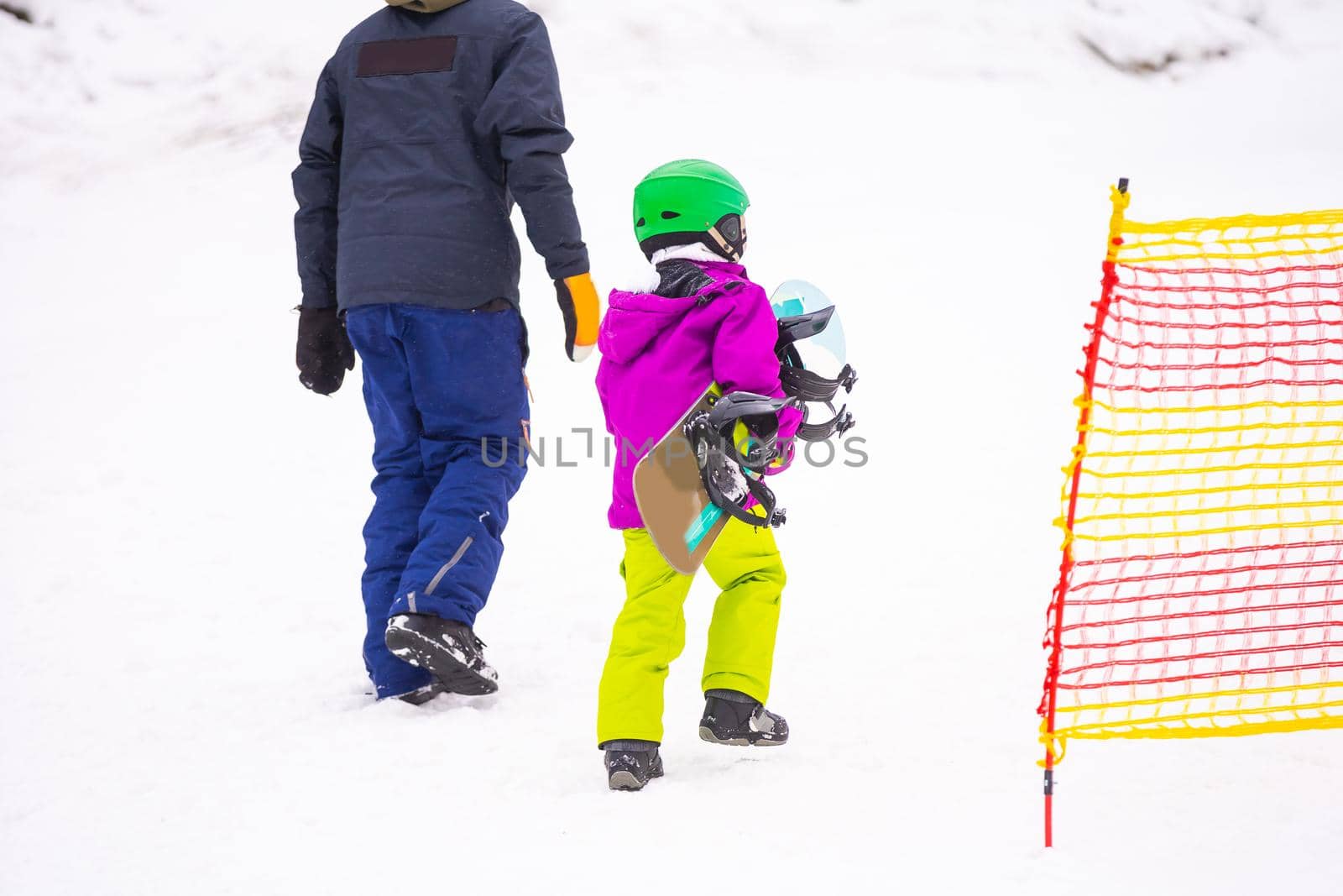 Instructors teach a child on a snow slope to snowboard