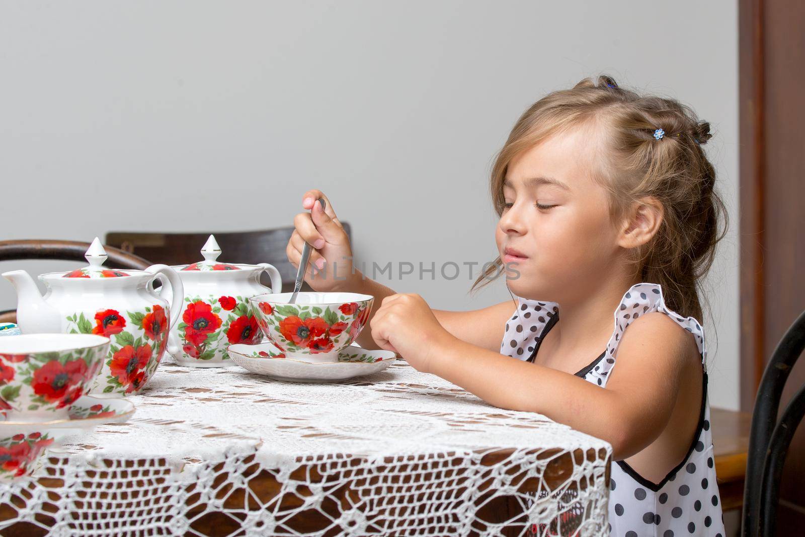 A little girl is drinking tea at the table. Stylized as a room of the fifties of last century. Retro style.