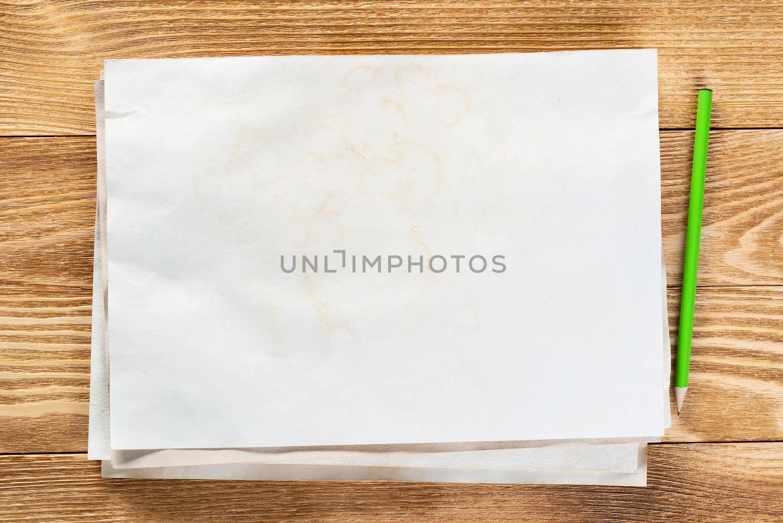 Artist workplace with sheet of paper and pencil lying on wooden desk. Rectangular white paper stack with blank copy space. Textured natural wooden background. Art school template for advertising