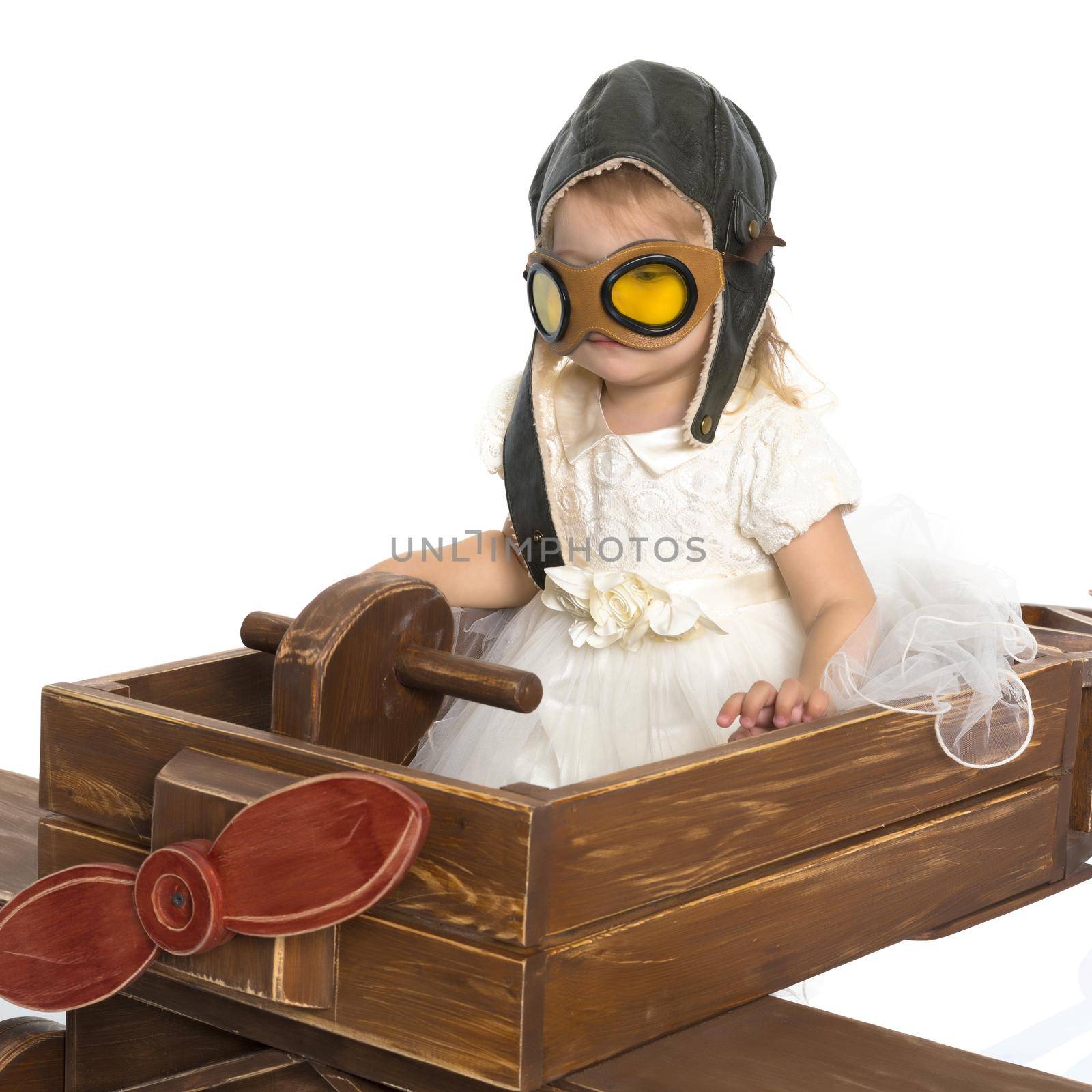 A little girl in a pilot's cap is playing in a large wooden plane. The concept of a happy childhood, games in the family and in kindergarten. Isolated on white background.