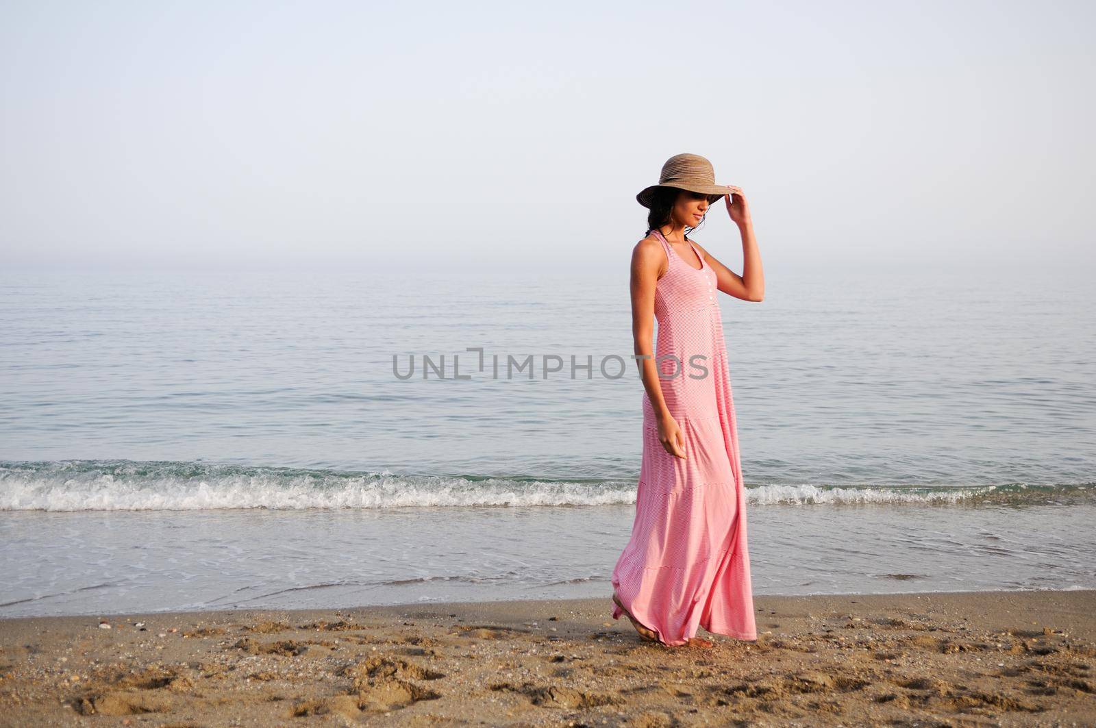 Portrait of a beautiful woman with long pink dress and sun hat on a tropical beach