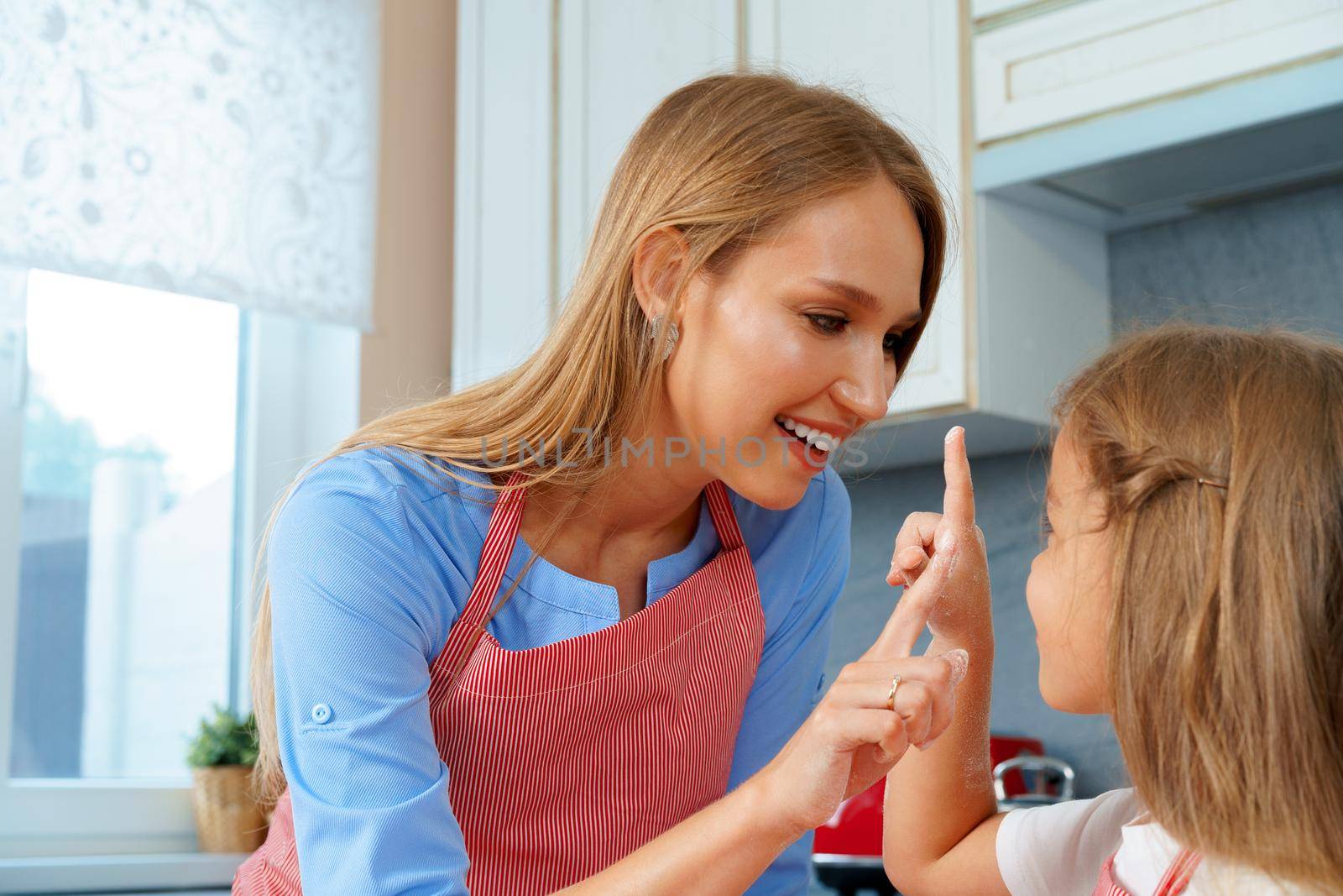 Beautiful mother and her adorable daughter having fun in the kitchen while cooking food at home