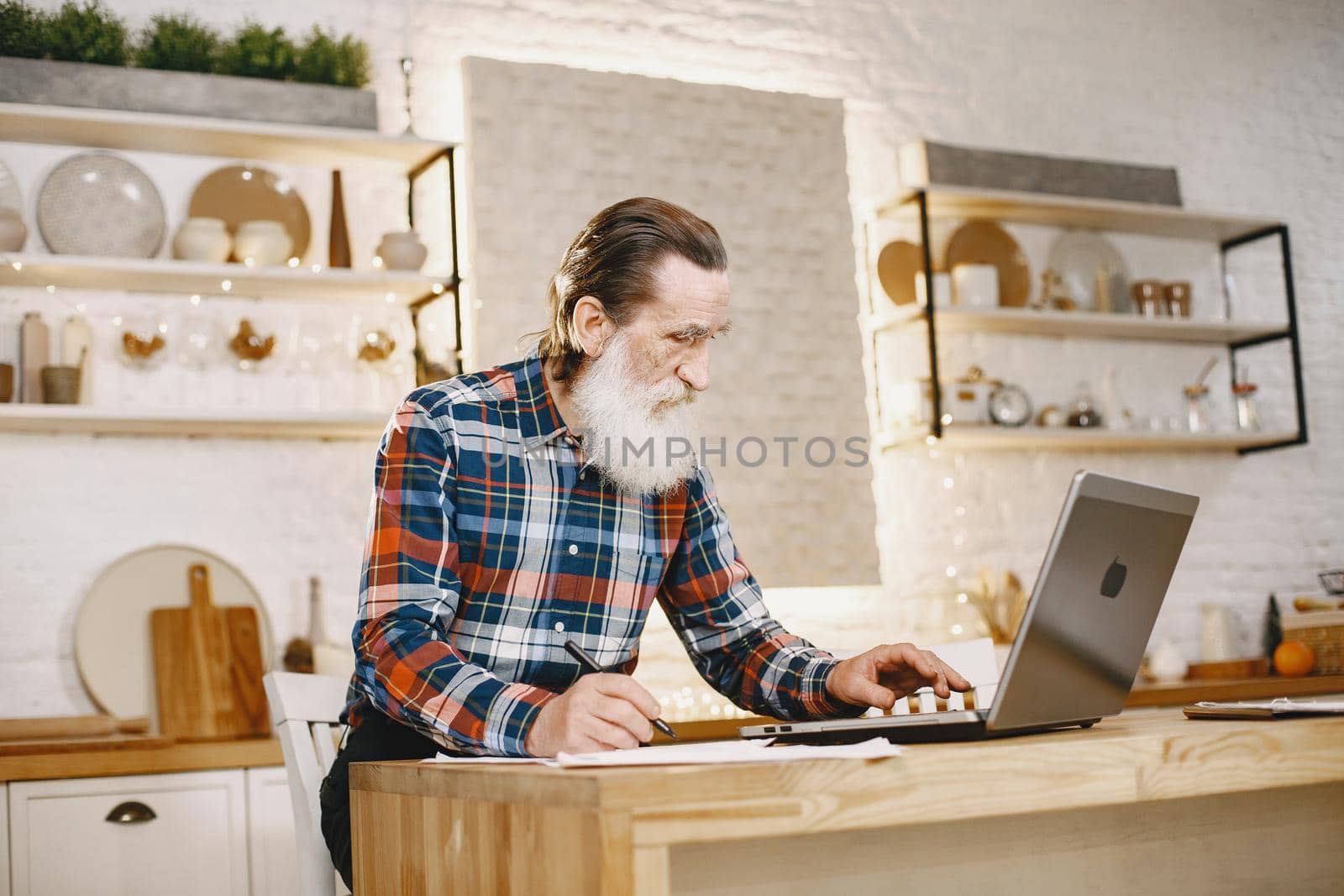 Old man with laptop. Grandfather sitting in a Christmas decorations. Man in a cell shirt.