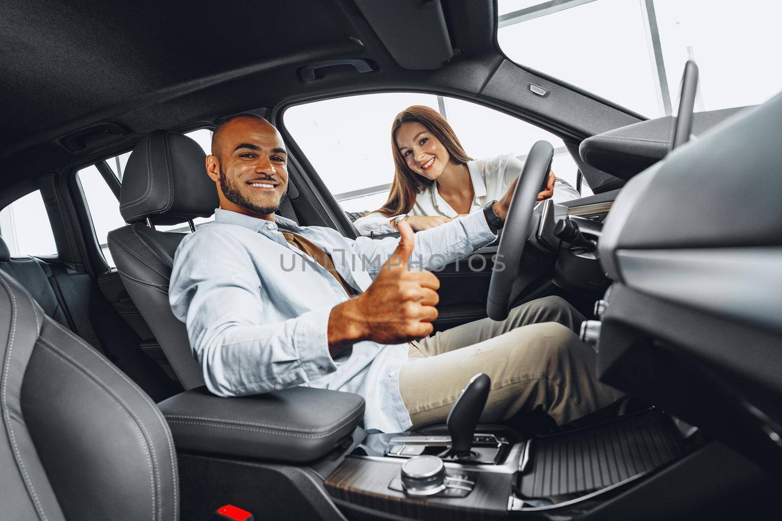 Young attractive caucasian woman salesperson in car showroom showing a car to her male African American client