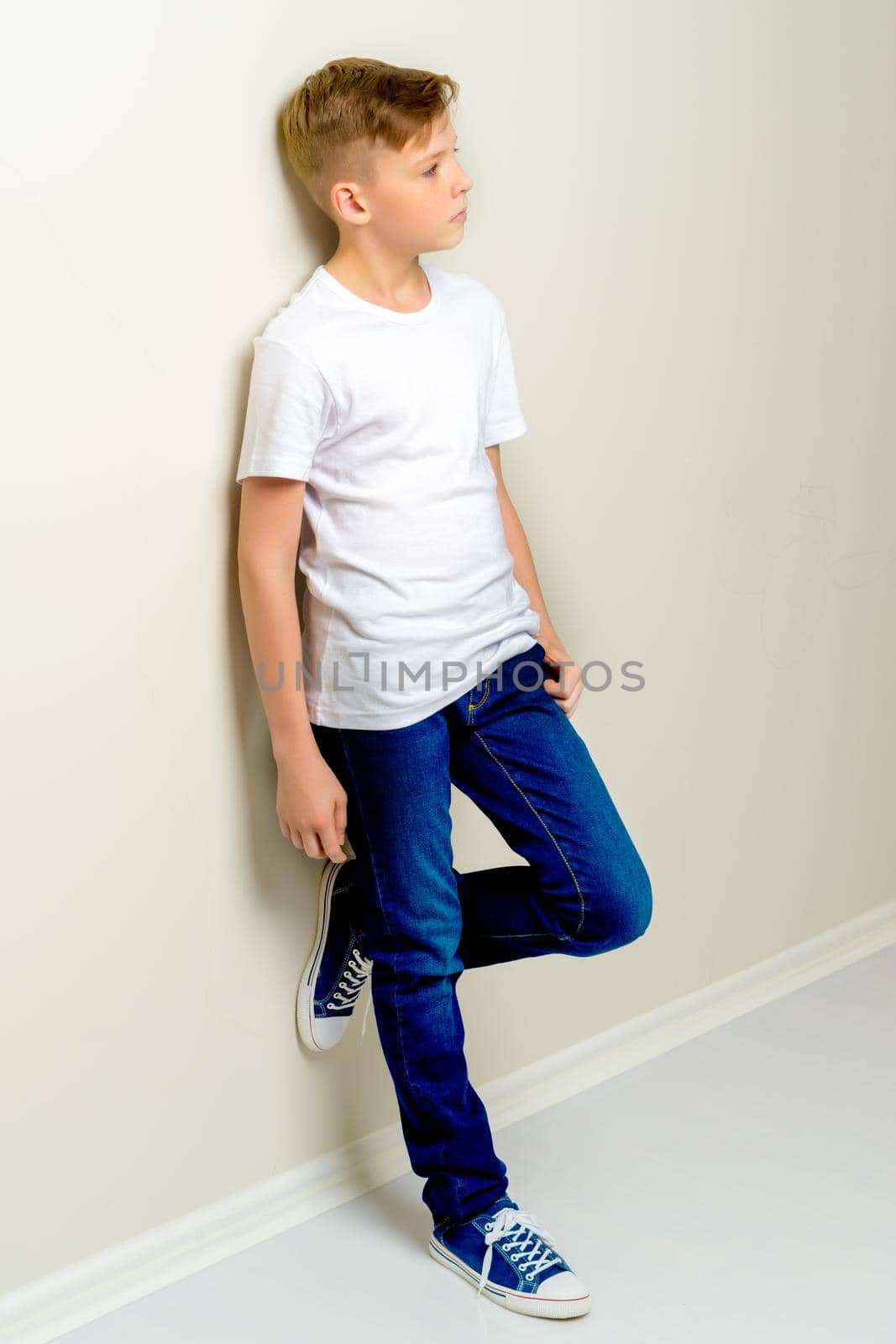 A handsome school-age boy leaned against the wall. The concept of youth fashion and culture.