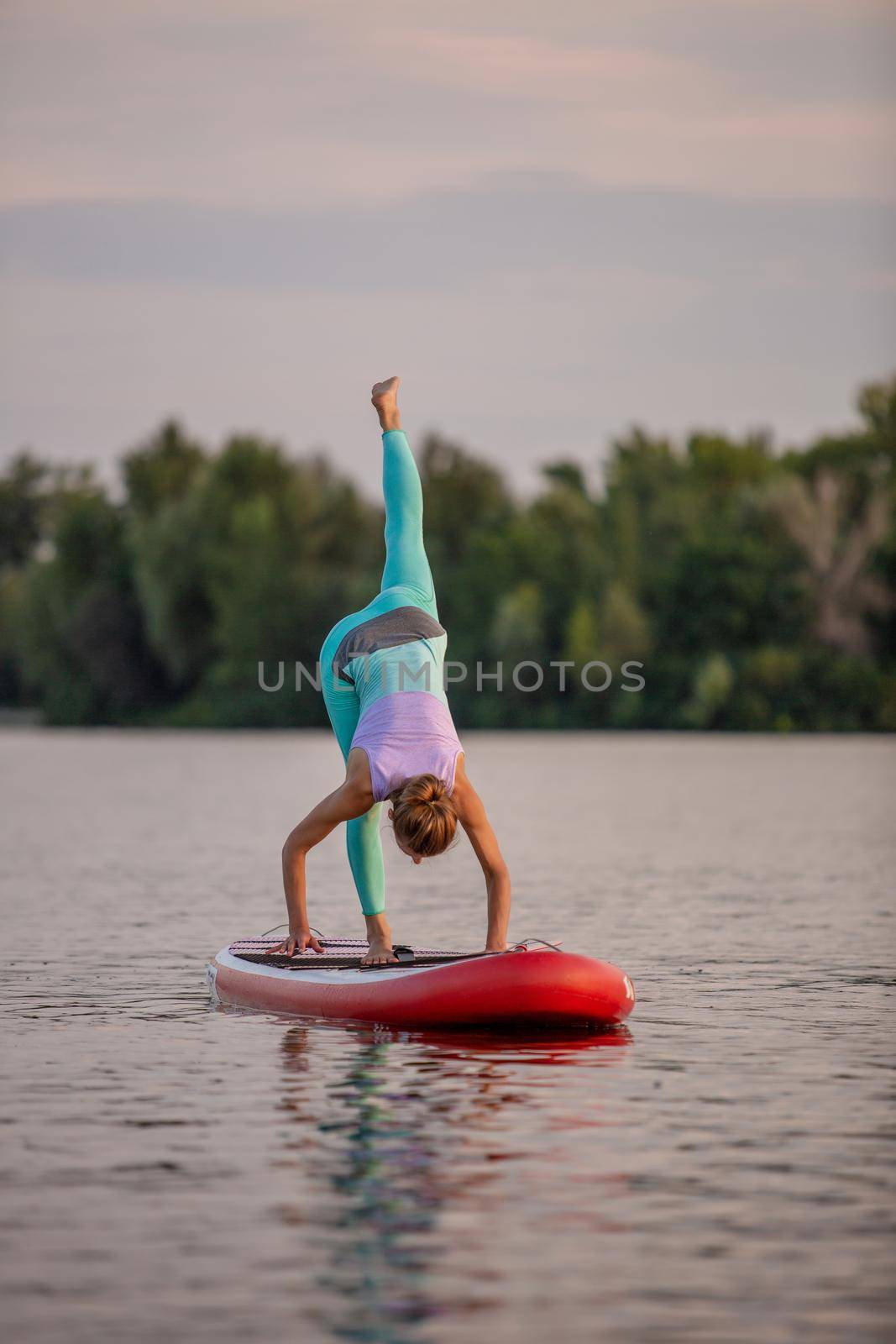 Sporty woman in yoga position on paddleboard, doing yoga on sup board, exercise for flexibility and stretching of muscles by nazarovsergey