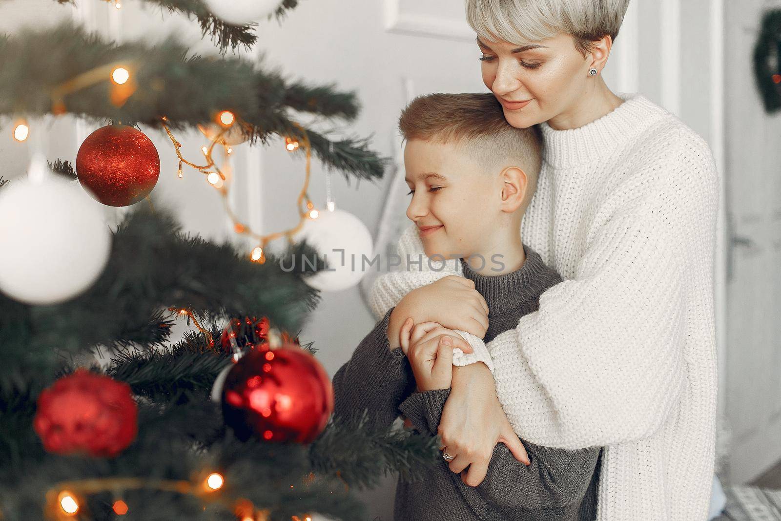 Beautiful mother in a white sweater. Family in a christmas decorations. Little boy in a room