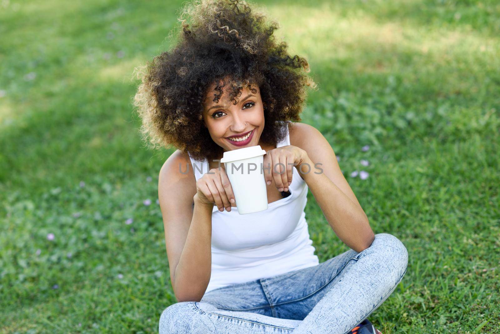 Woman with afro hairstyle drinking coffee in park by javiindy