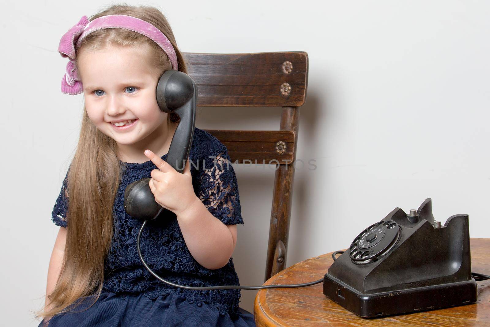 A sweet little girl is ringing on the old phone. The concept of a happy childhood, retro style, old things of the fifties of last century.