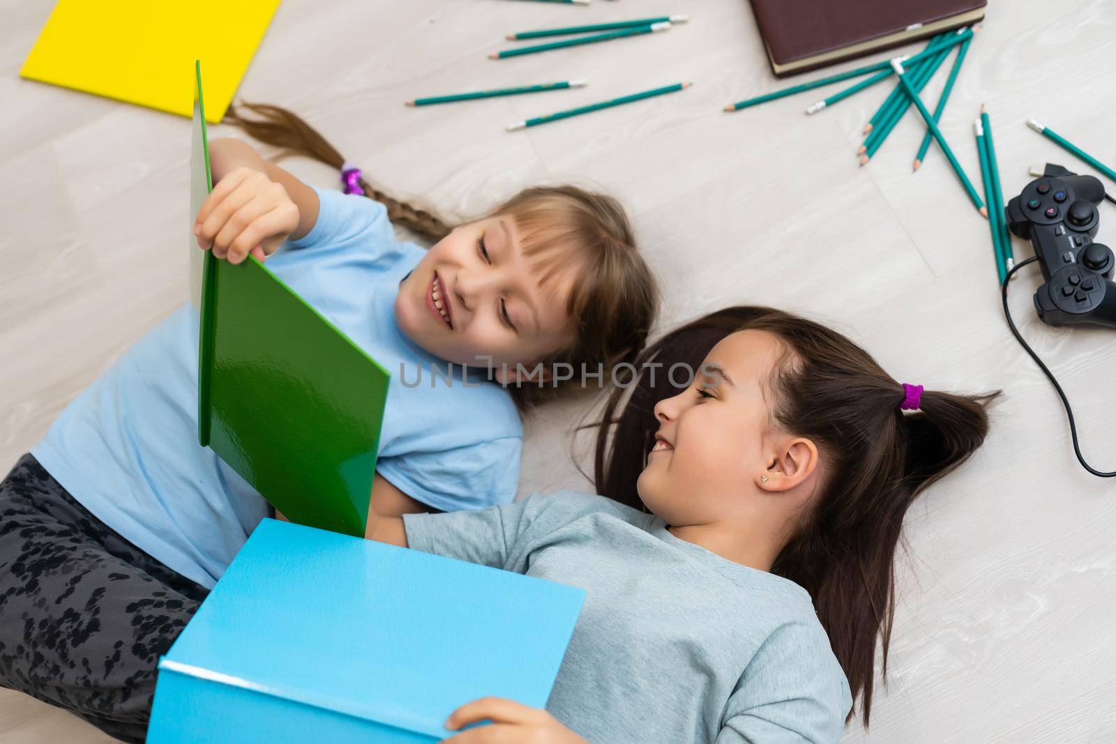 two little girls sisters reading a book lying on the floor by Andelov13