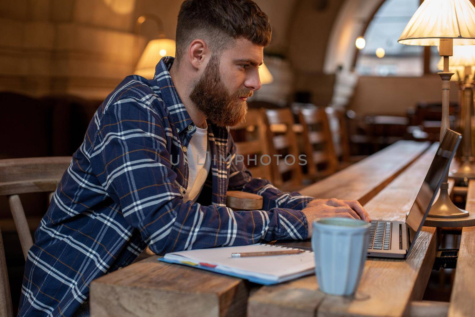 Young professional surfing the Internet on his laptop with cup of coffee on table at coffee shop or home office, working from cafe concept