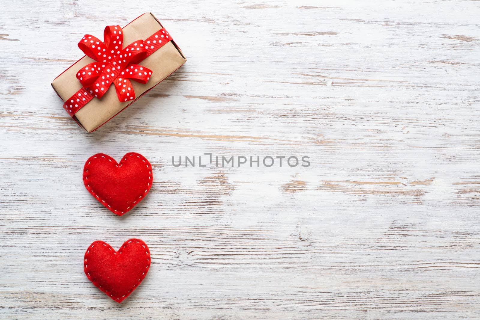 Flat lay cute composition with handmade fabric red hearts. Gift box with ribbon bow on wooden table. Happy birthday or anniversary congratulation. Romantic message template with copy space.