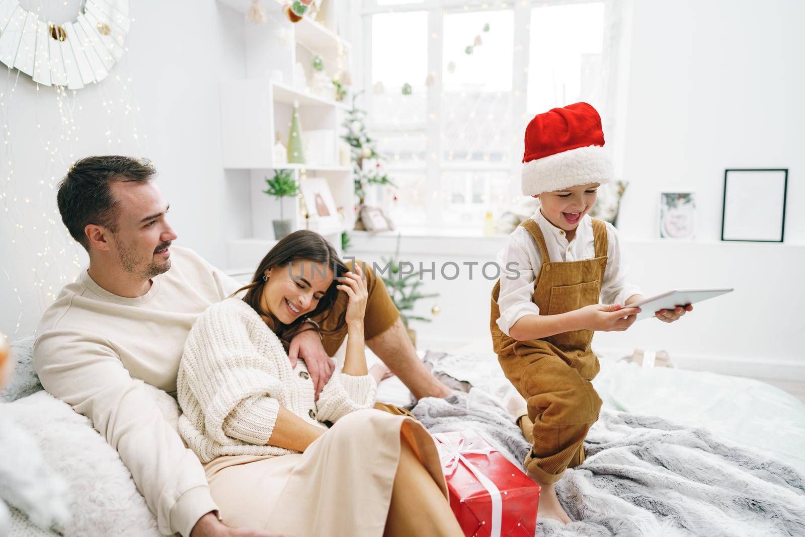 Happy family having fun on digital tablet in bed on Christmas by Fabrikasimf