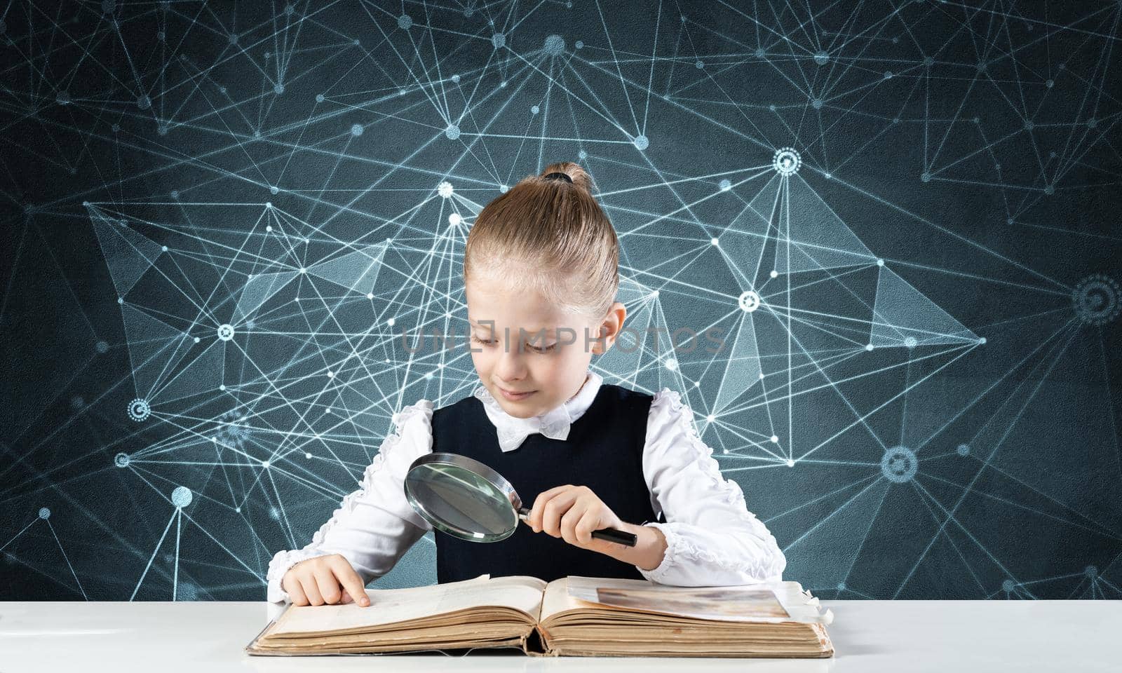 Little girl sitting at desk with magnifier and open book. Research and education in school. Happy schoolgirl in school wear carefully studying book. Clever girl reading book with magnifying glass.