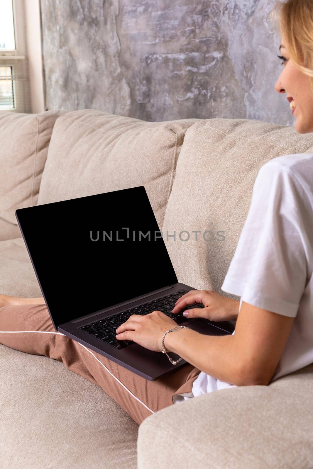 Woman on sofa working on laptop with mockup blank screen. Empty copy space on monitor for advertisement. Black screen. by nazarovsergey