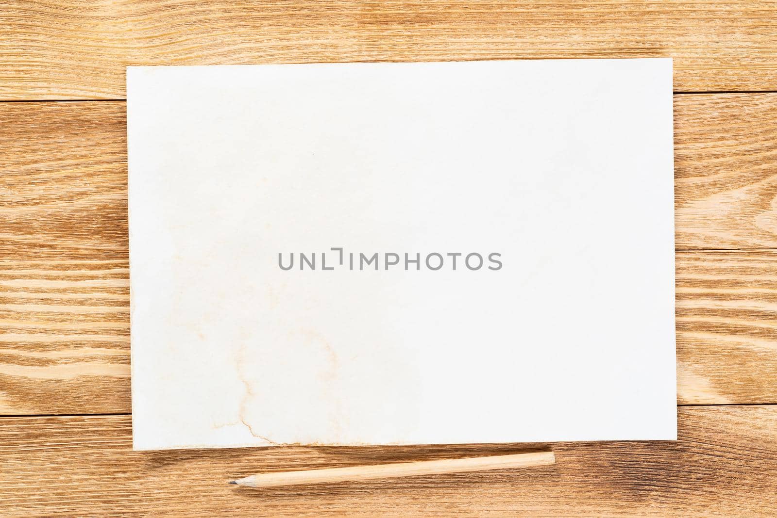 Sheet of paper lying on wooden table. Blank white a4 format paper with pencil. Textured natural wooden background. Vintage copy space for design. Business planning and idea generation.