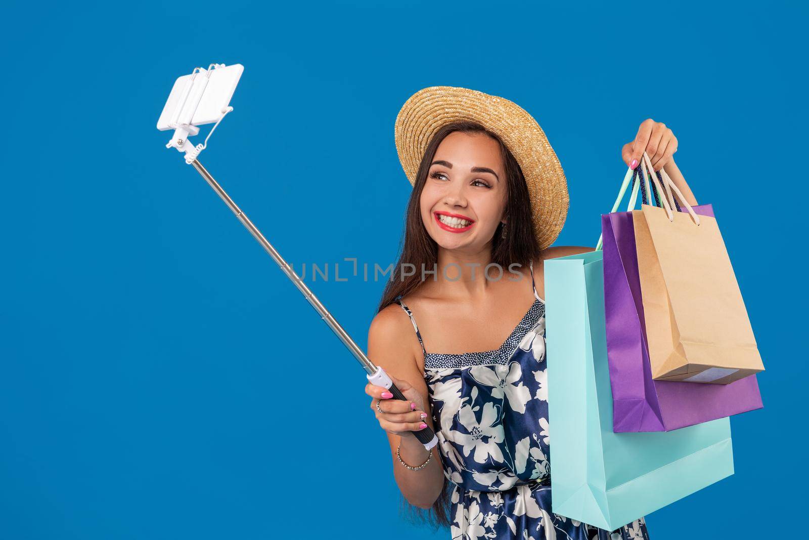 Young stylish woman posing and taking a selfie on the phone with shopping bags on a blue background. Emotions. Purchases. Sale. Shopping