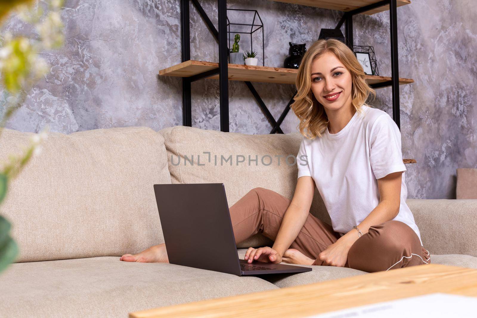 Young beautiful woman using laptop computer smiling happy watching and browsing or doing online internet shopping at home. Modern living room. Cheerful and satisfied face expression