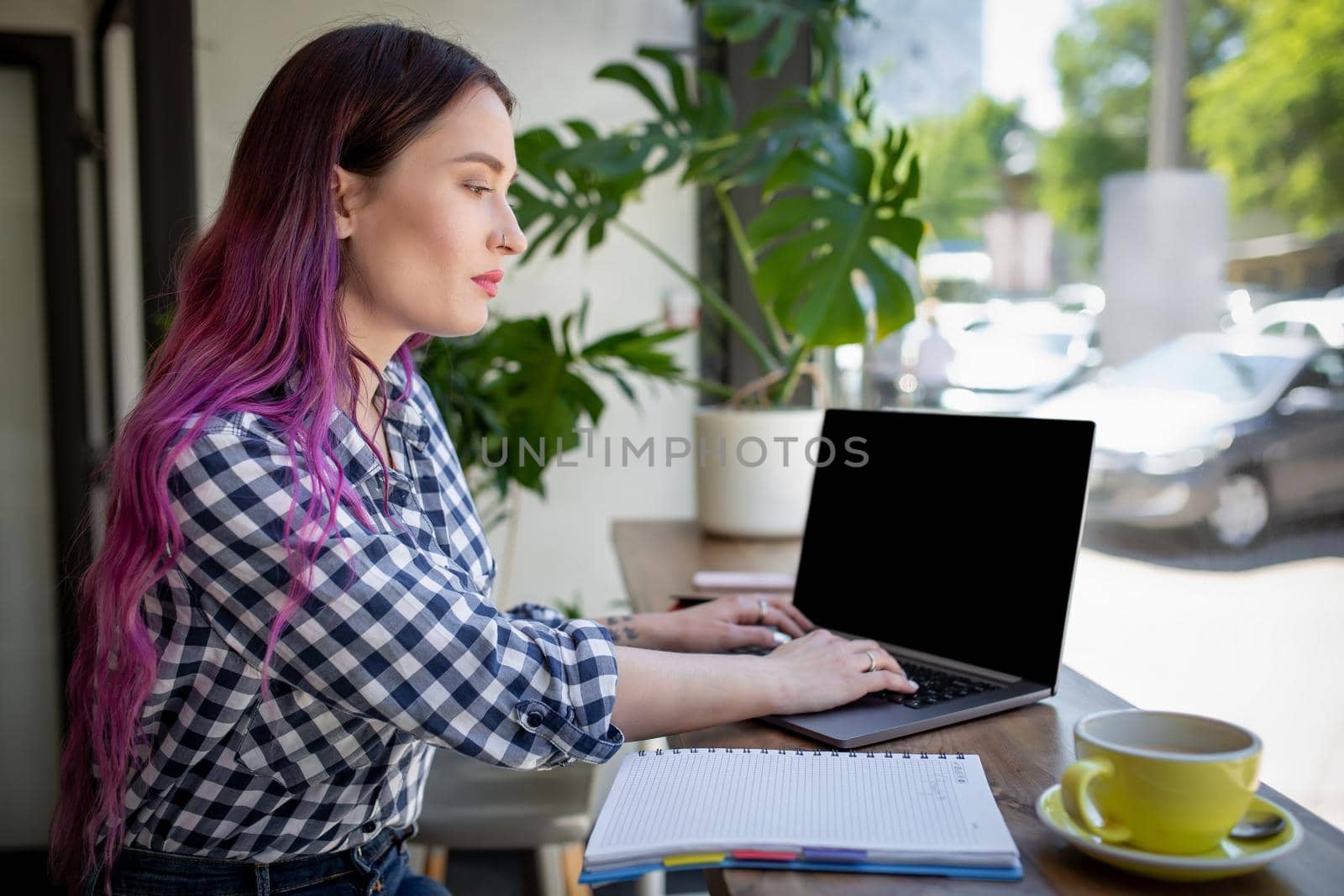 Rear shot of female student learning online via laptop before her lectures. Woman typing on notebook with blank screen with copy space for your text or advertising content, sitting at wooden table