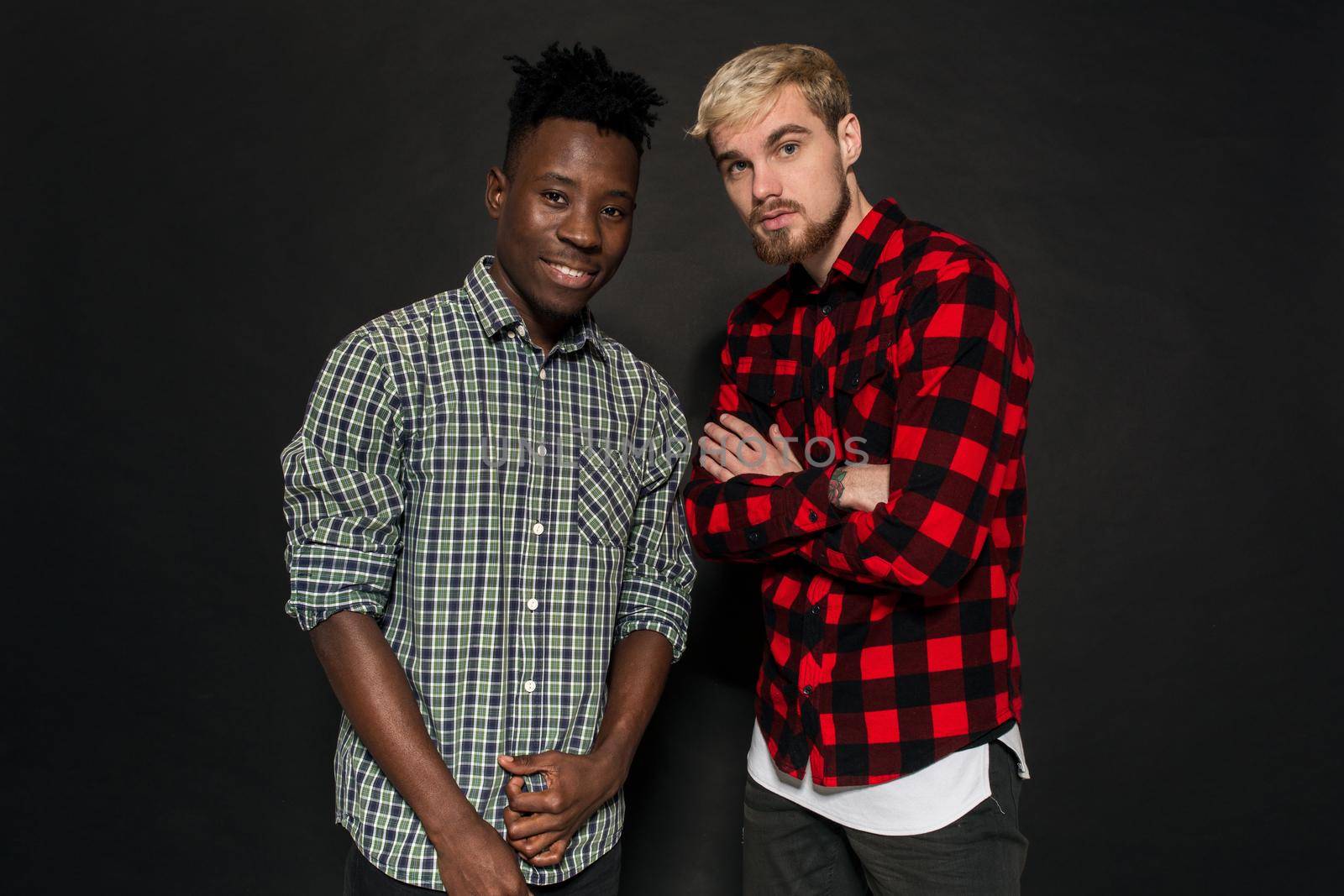 Studio shot of two stylish young men having fun. Handsome bearded hipster in a shirt in a cage standing next to his African-American friend against a dark background. by nazarovsergey