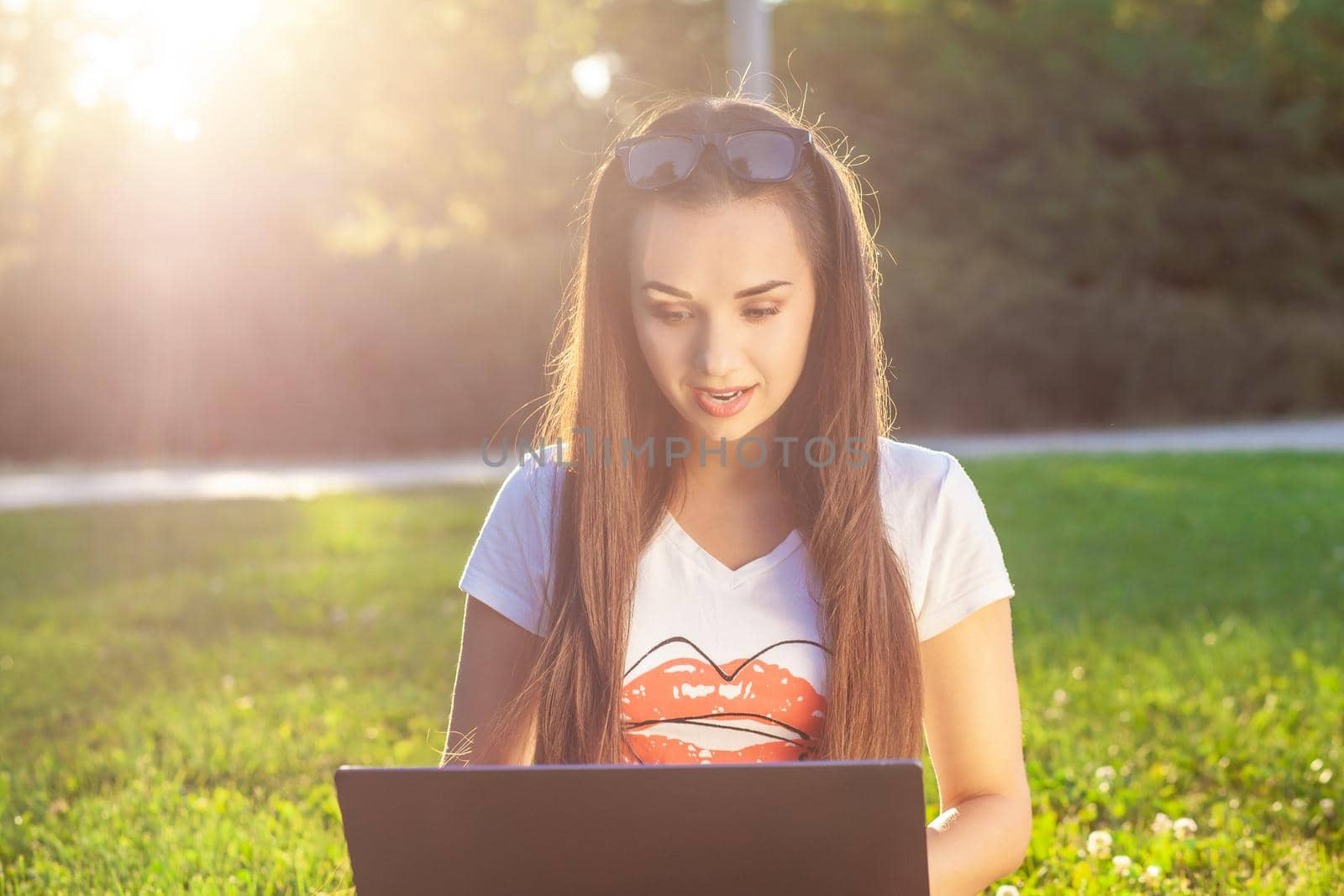 Young woman using computer on green grasses in the park. Education learning or freelance working outdoor or relaxation concept idea background. Modern lifestyle, information technology or online shopping concept