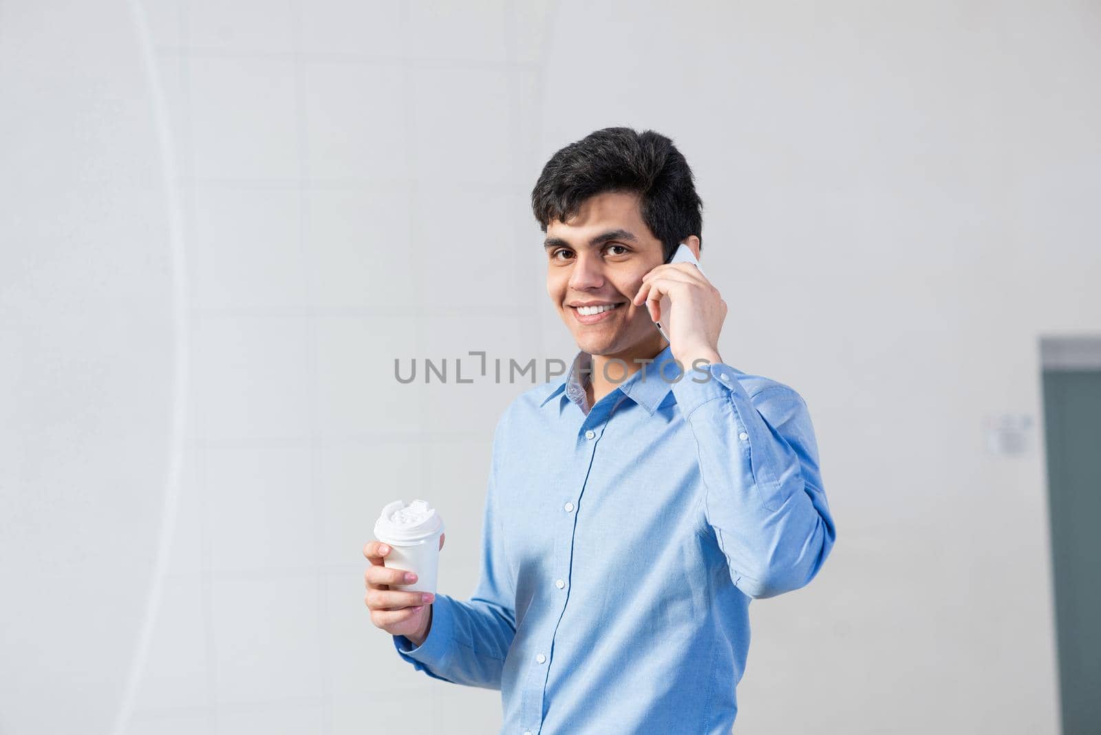 a young businessman talking on his cell phone. holding a paper cup of coffee