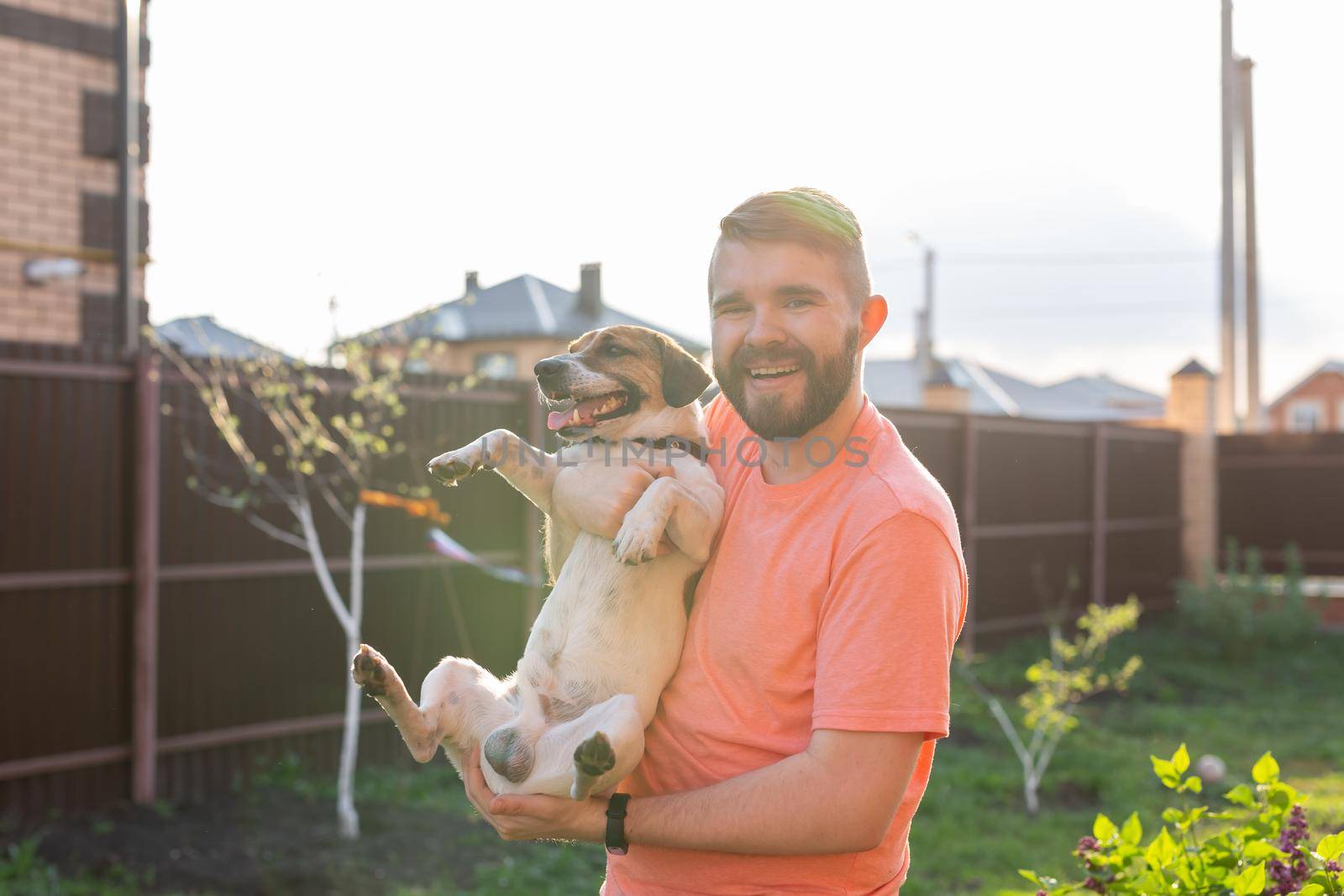 People, pets and dogs concept - young man hugging funny Jack Russell Terrier outdoors.