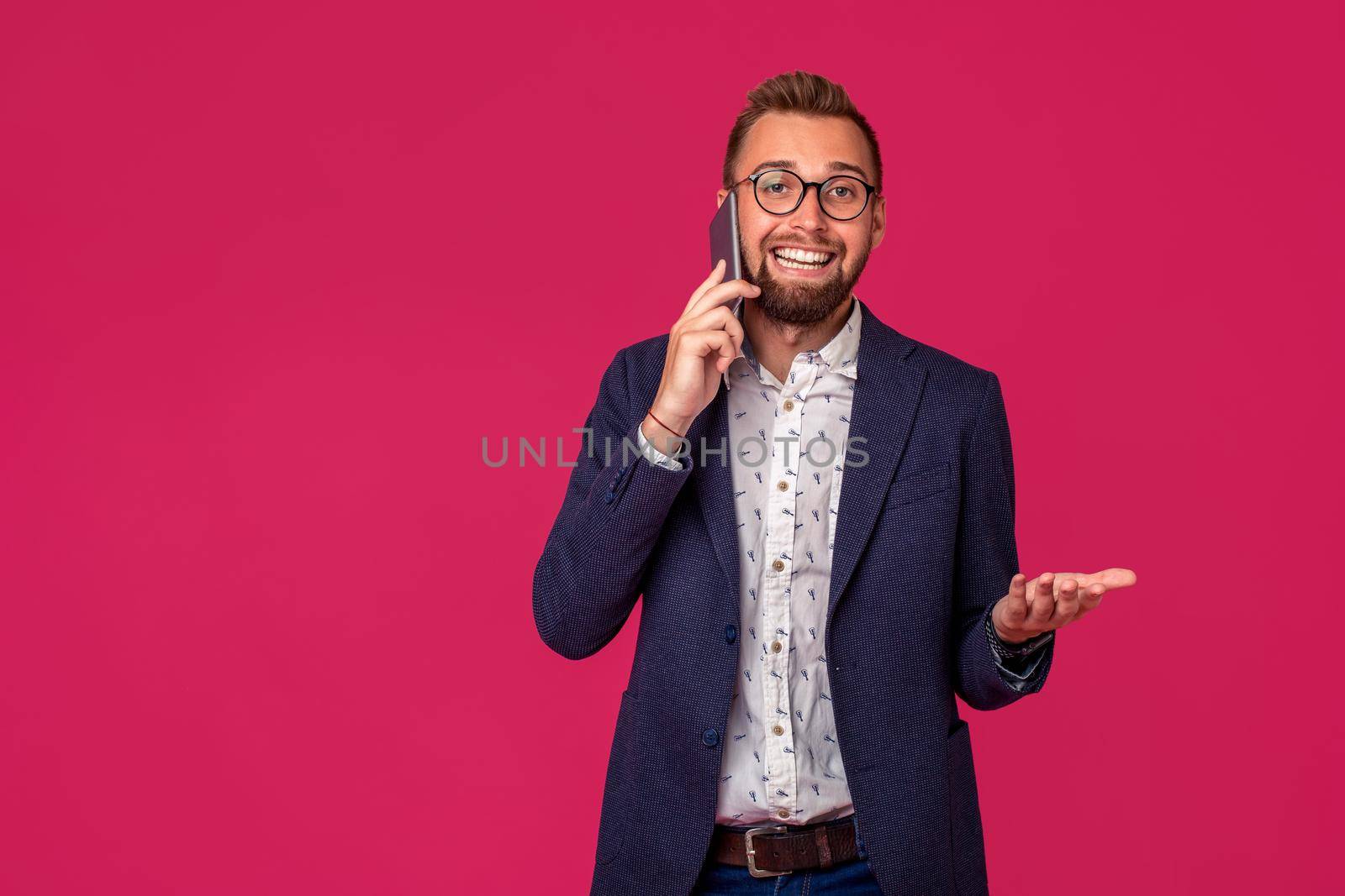Young cheerful lawyer or businessman is standing on the pink background and smiling,talking on the phone, wearing jacket, shirt and jeans. Copy space