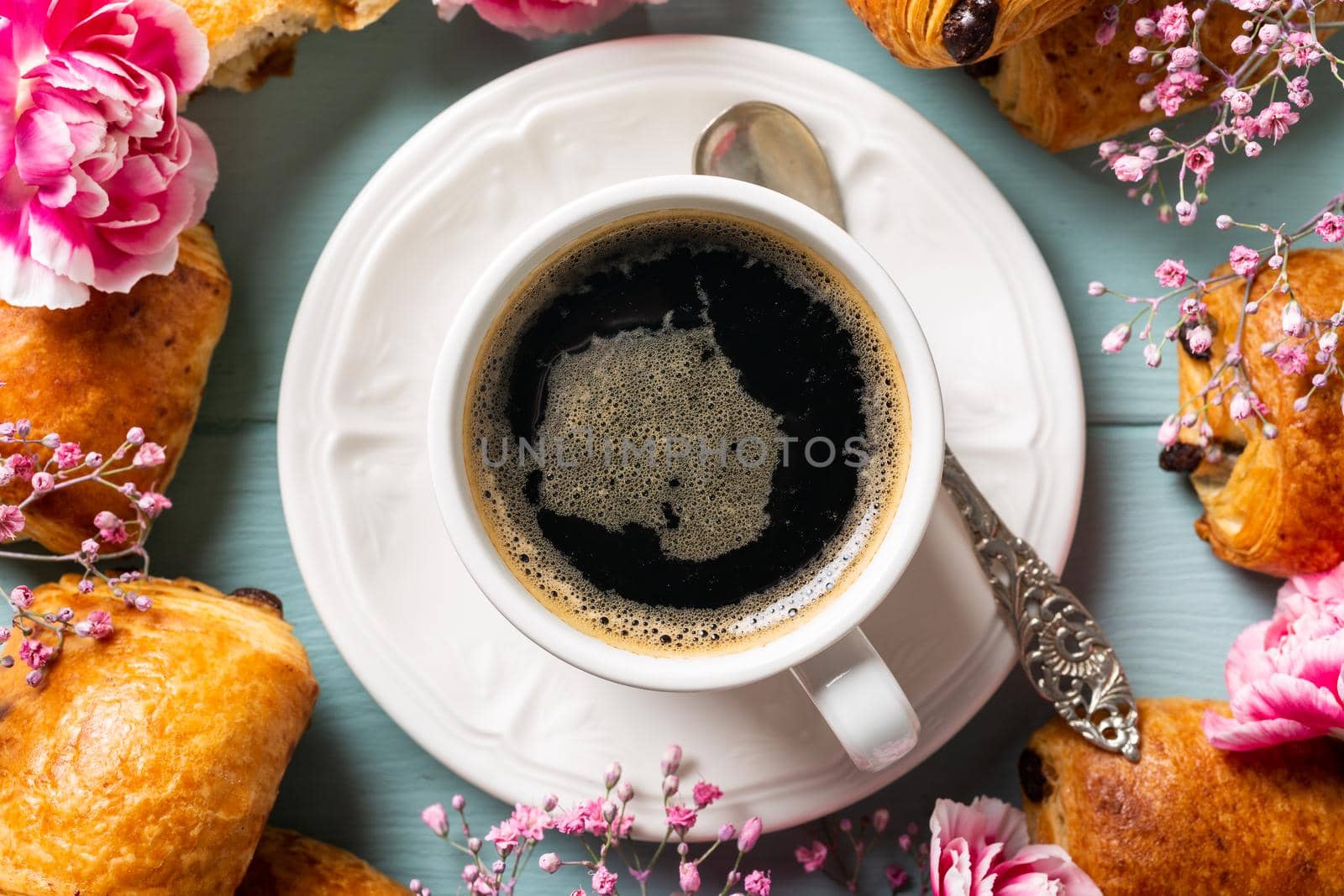 Holiday flat lay with cup of coffee, mini fresh croissants chocolate bun and carnation flowers on turquoise background. Top view.