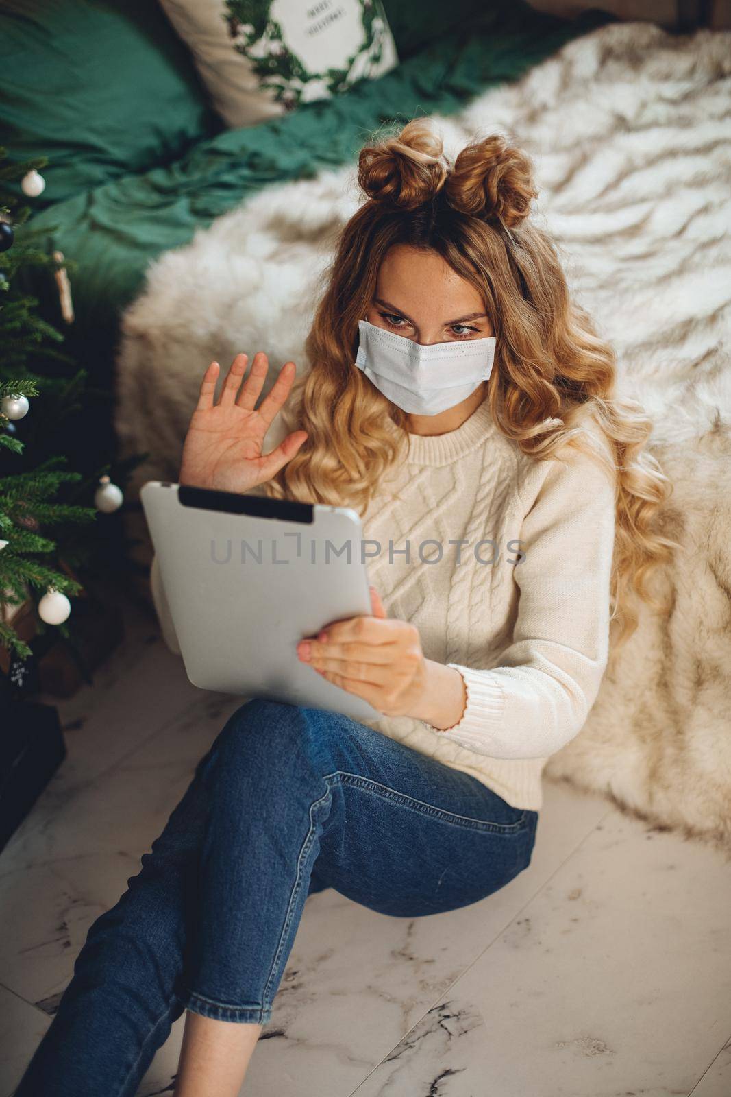 caucasian girl with medical mask on her face wishes happy new year to her family with a tablet