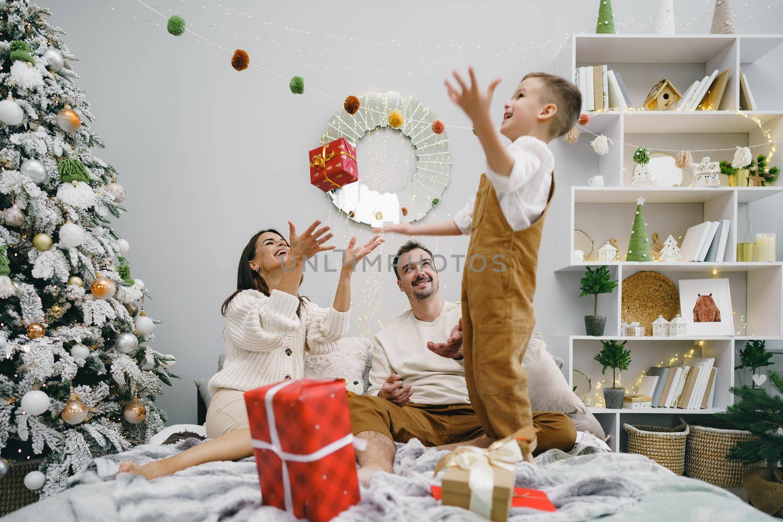 Mother, father and son having fun together on bed on Christmas day