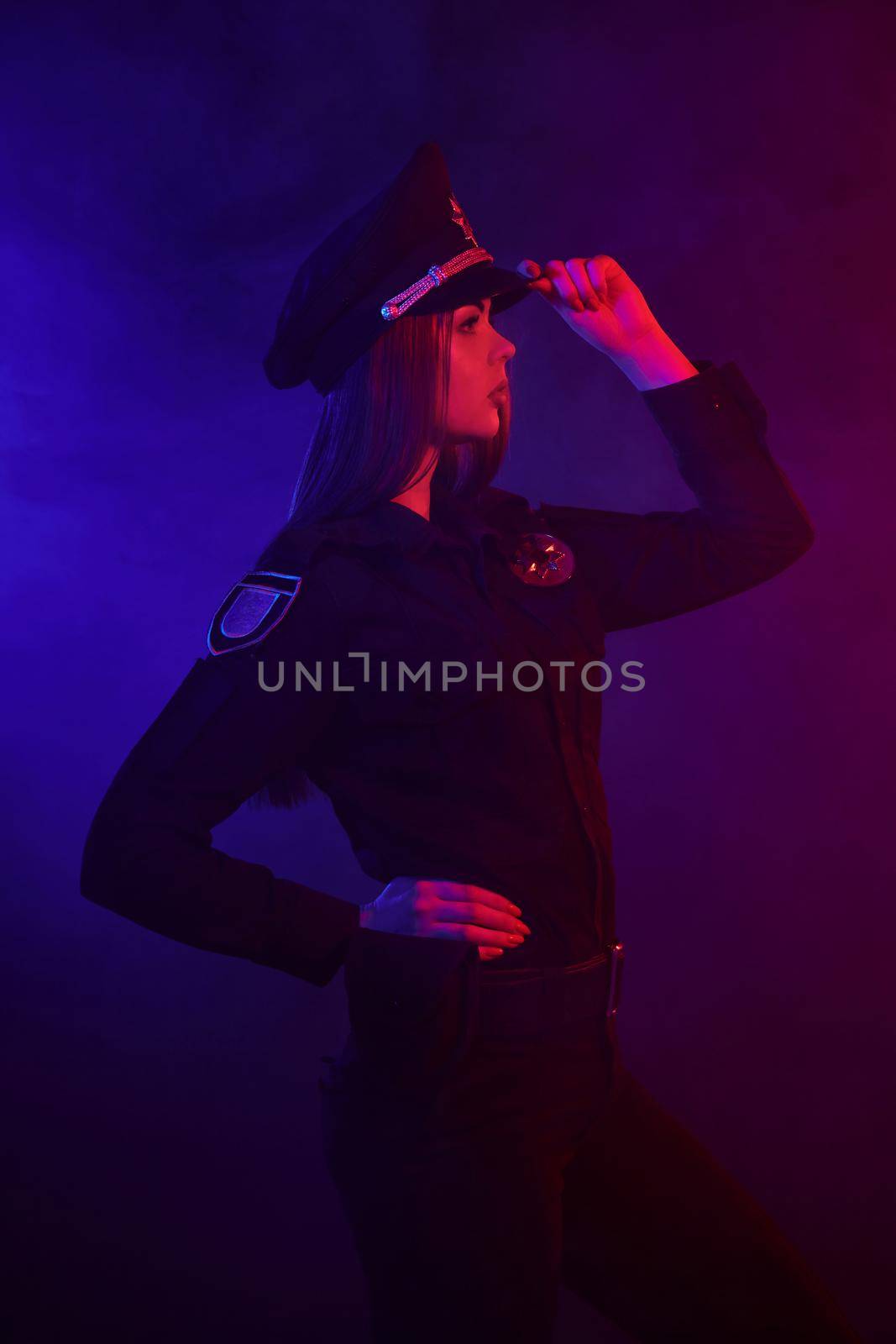 Redheaded female police officer is posing for the camera against a black background with red and blue backlighting. by nazarovsergey