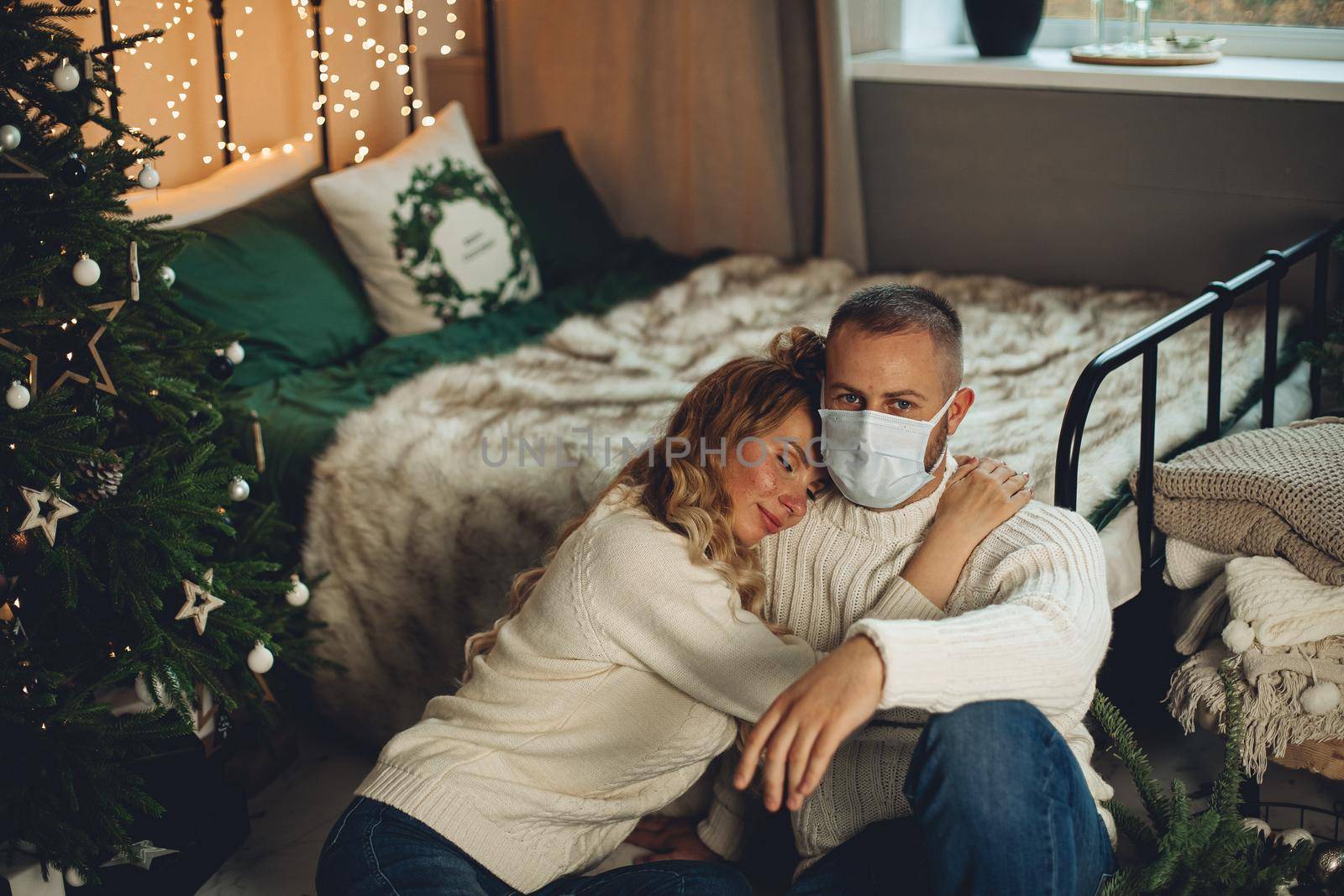 Beautiful couple in love sits on the floor near the christmas tree during the quarantine by StudioLucky