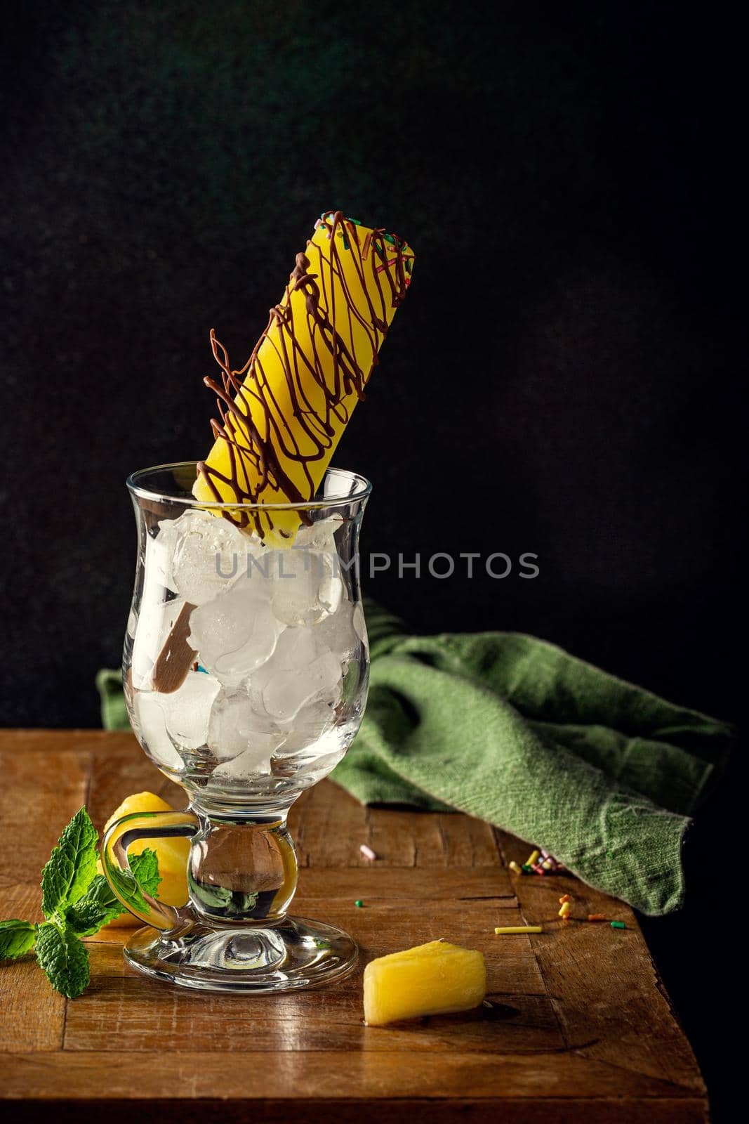 Delicious homemade pineapple in chocolate popsicle in glass on wooden table. Summer food concept with copy space. Dark photo