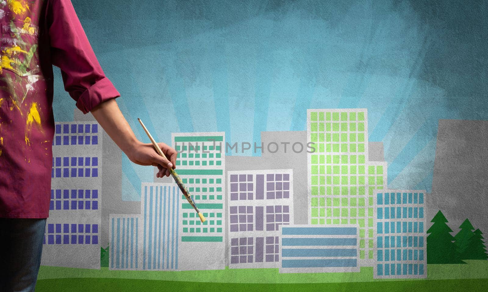 Close up artist hand holding paintbrush. Painter in shirt standing on background colorful picture of city. Modern cityscape with high skyscrapers artwork. Creative hobby and artistic occupation.