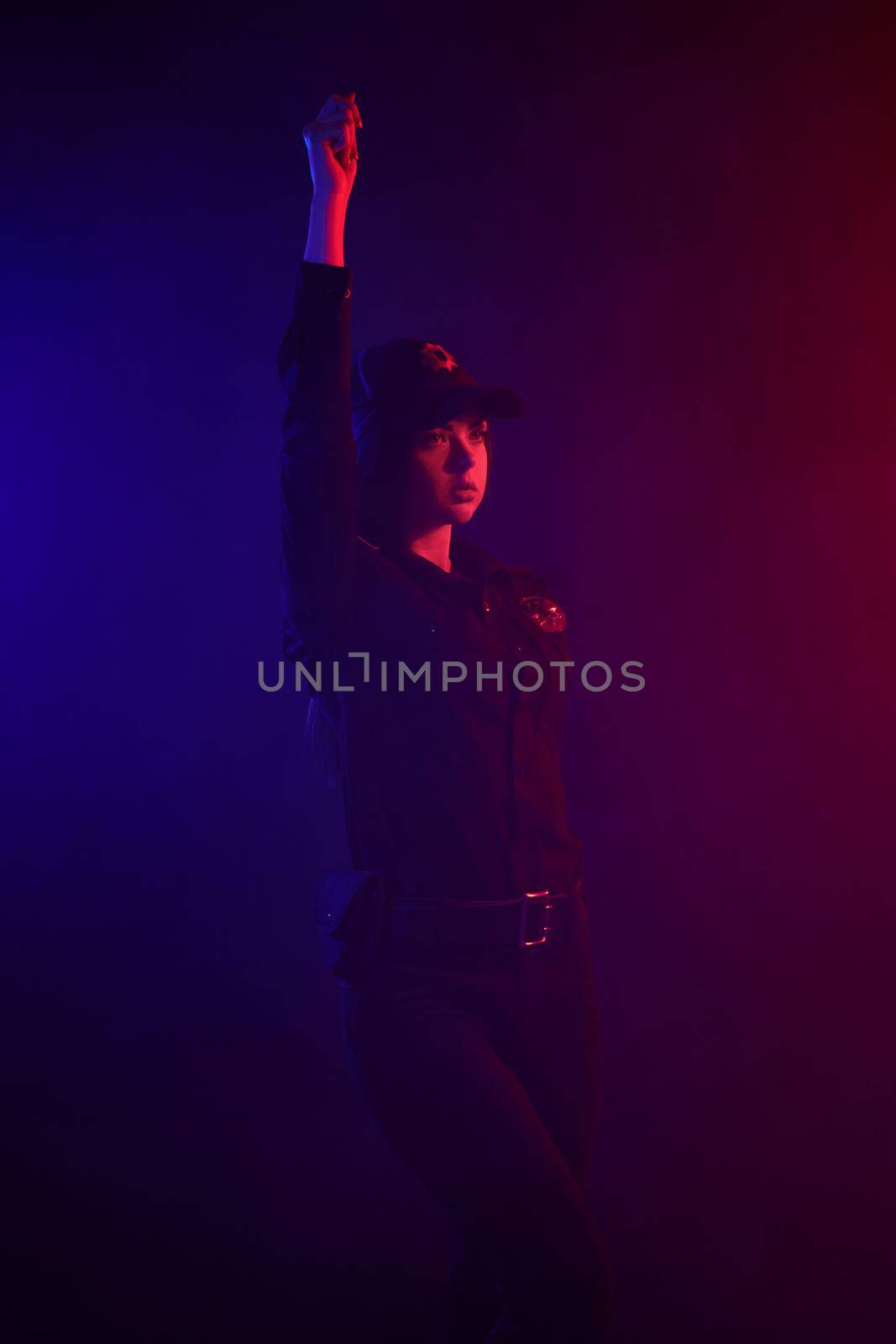 Redheaded female police officer is posing for the camera against a black background with red and blue backlighting. by nazarovsergey