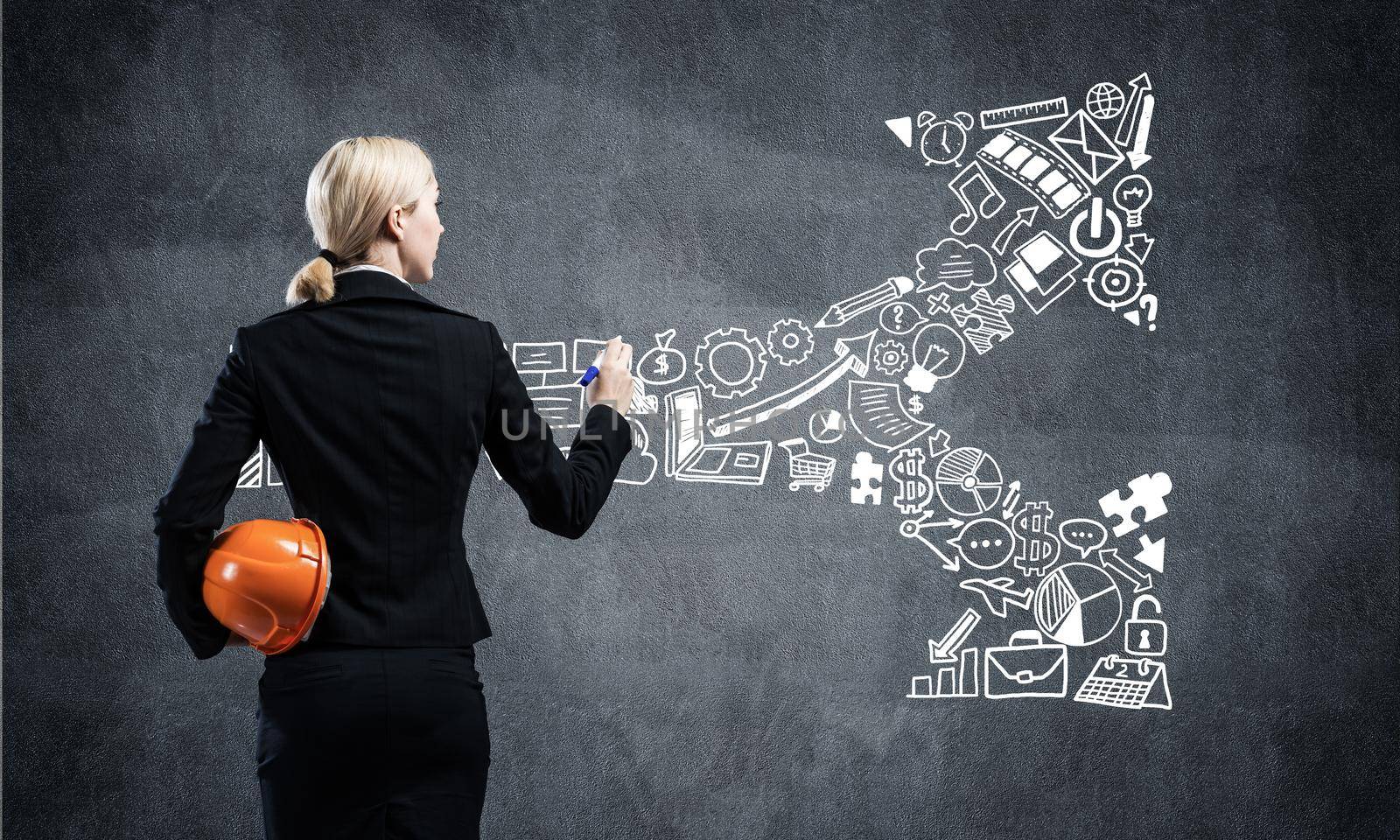 Businesswoman draws arrows consists of business doodles on blackboard. Personal success and career ambition. Back view woman with safety helmet. Strategy planning and project management concept.