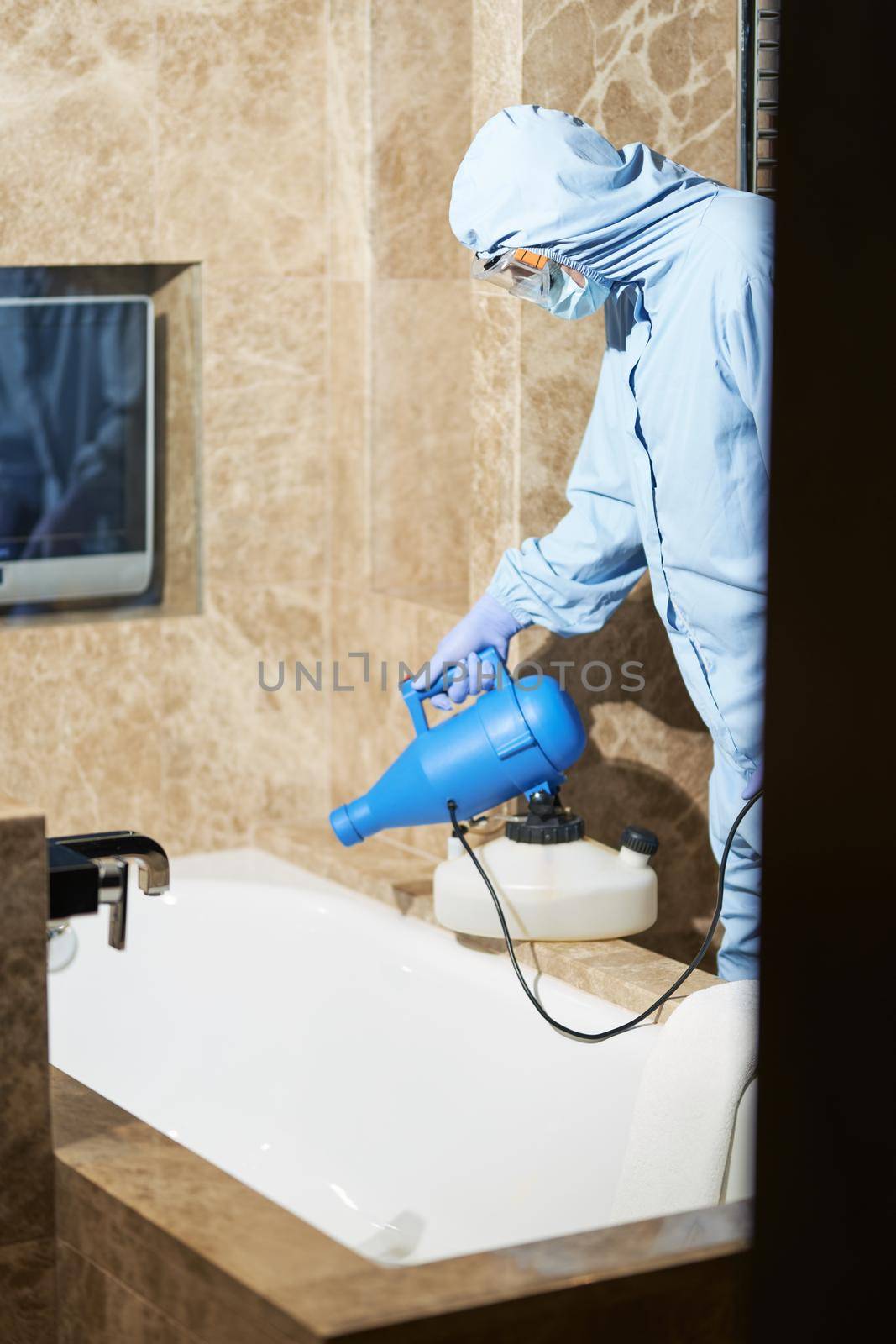 Technician in protective suit and glasses sanitizing a hotel bathroom by friendsstock