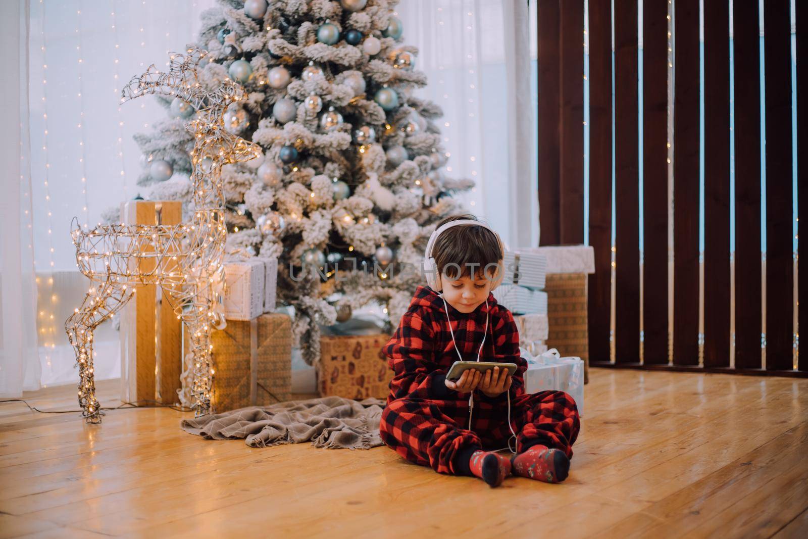 The boy with the phone under the Christmas tree lifestyle. New Year and Christmas. Festive decoration.