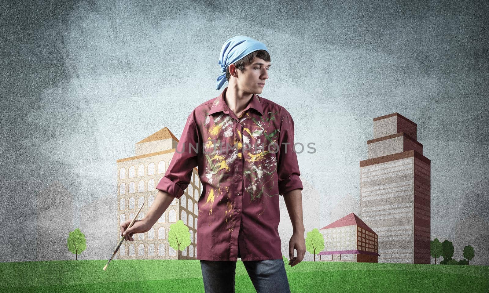 Young male artist holding paintbrush. Painter in shirt and bandana standing on background colorful picture on wall. Modern cityscape with high skyscrapers artwork. Creative hobby and profession
