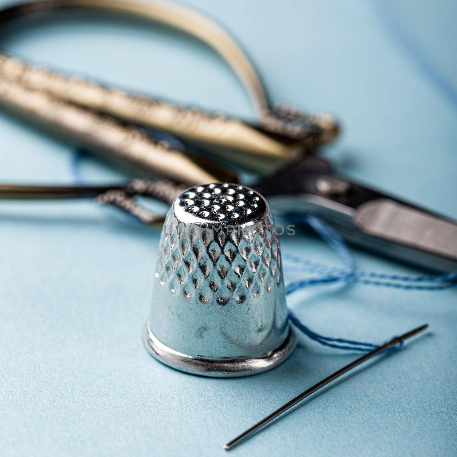 Vintage silver metal thimble and needle, scissors on blue background