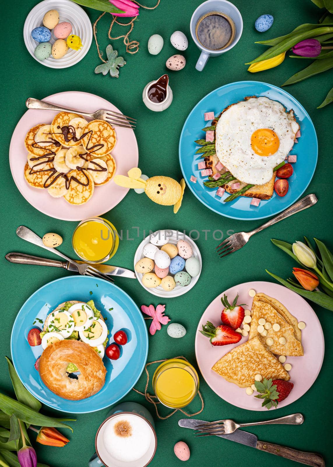 Easter composition with breakfast flat lay with scrambled eggs bagels, tulips, pancakes, bread toast with fried egg and green asparagus, colored quail eggs. Top view.