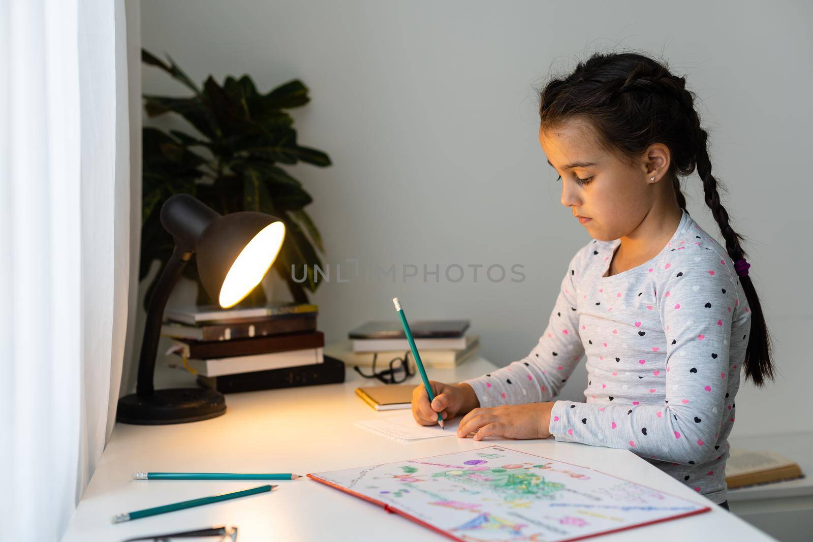 a child girl doing homework writing and reading at home by Andelov13